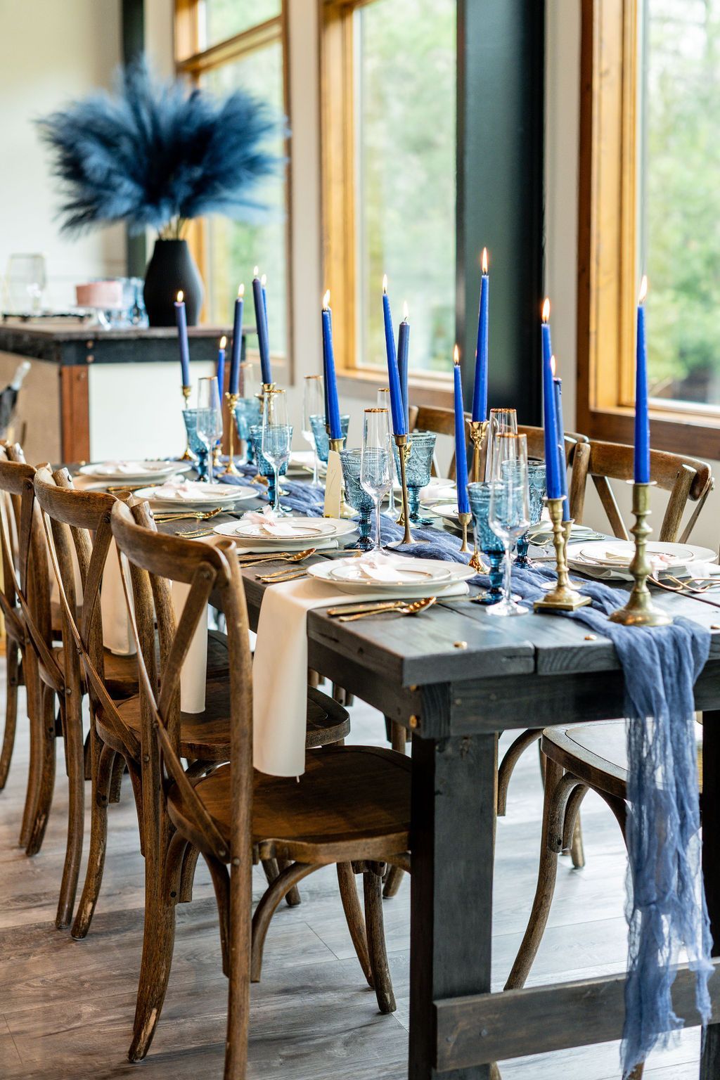 Elegant dining table set with blue candles and decor beside tall windows