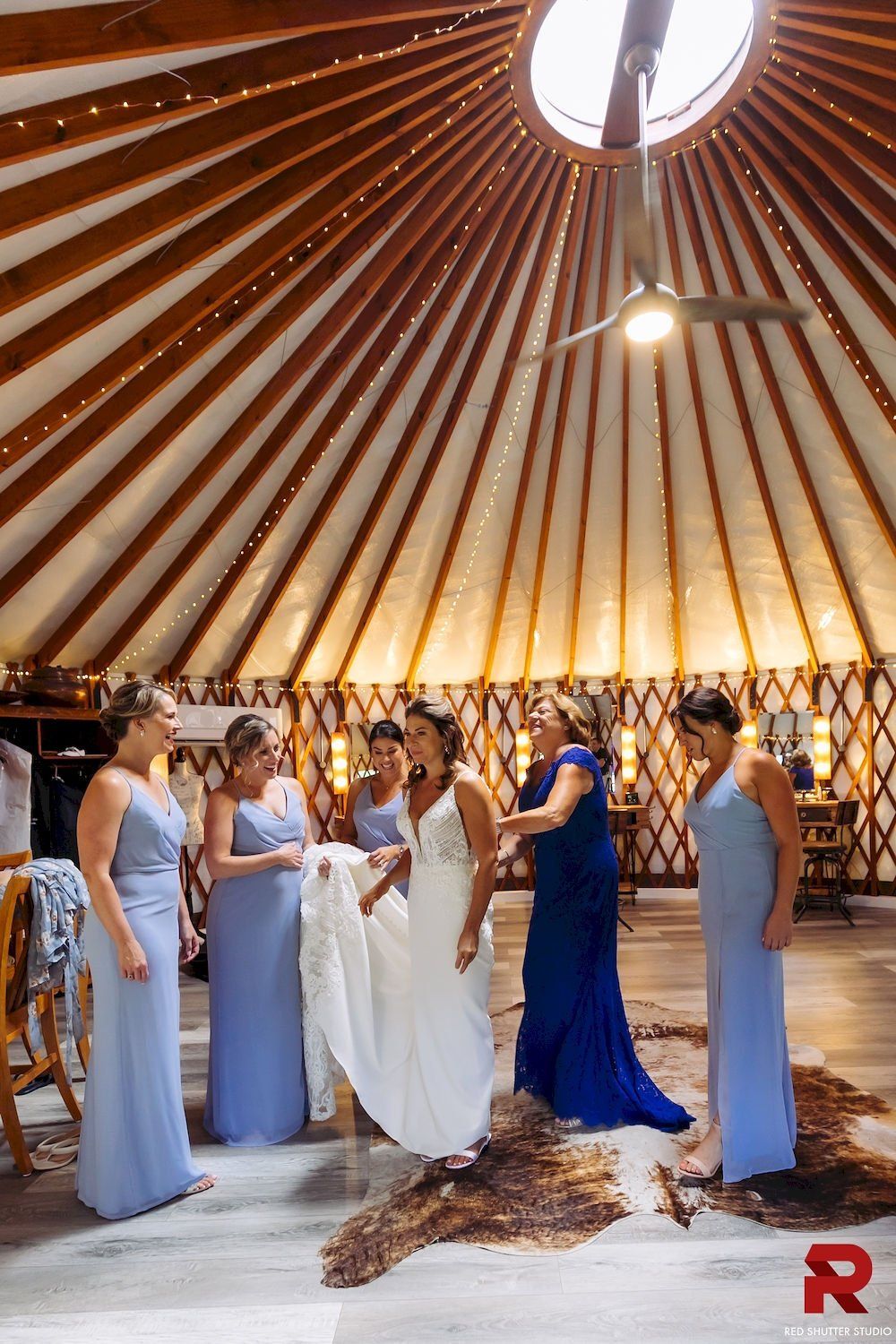Bridal party in lavender and blue dresses gathered in a wooden pavilion with a bride in white gown