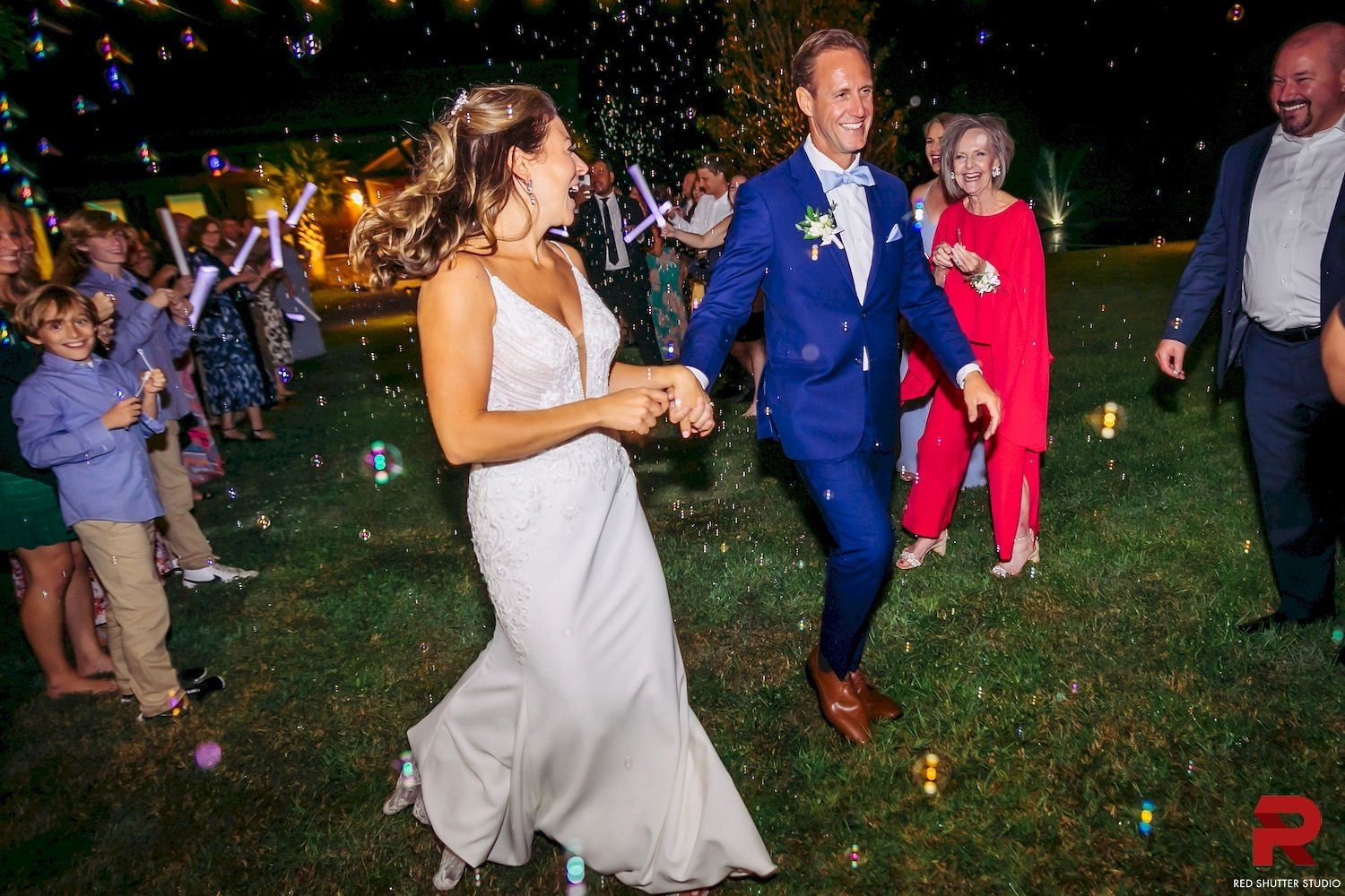 Couple dancing outdoors at a night wedding, with guests and sparklers in the background