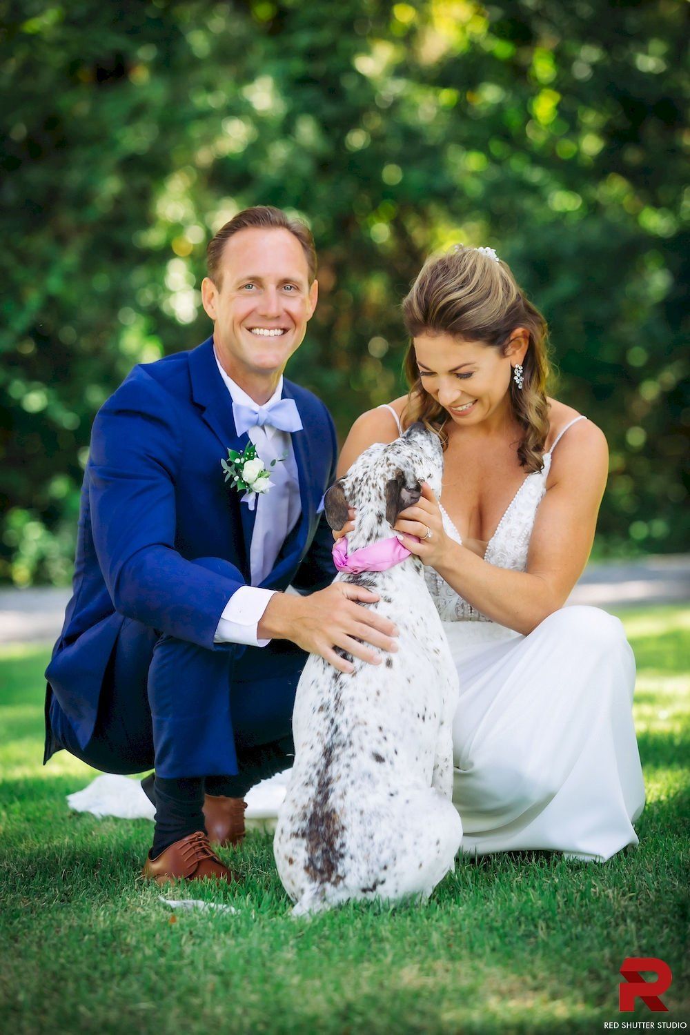 Couple kneeling on grass with a small dog in a garden, smiling and petting it