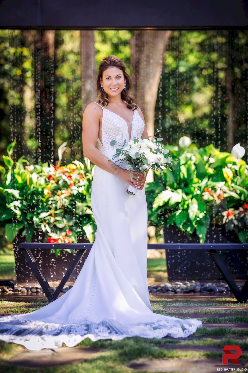 Bride in a white gown holding a bouquet in a garden setting with greenery and trees