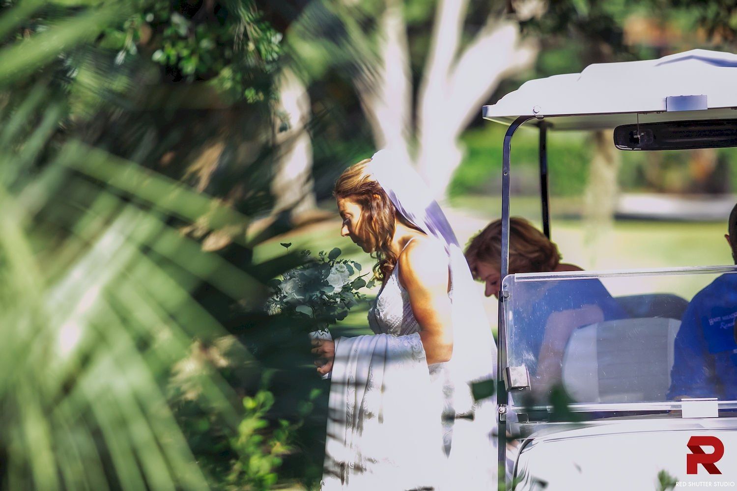 Person riding in a white golf cart beside palm trees outdoors