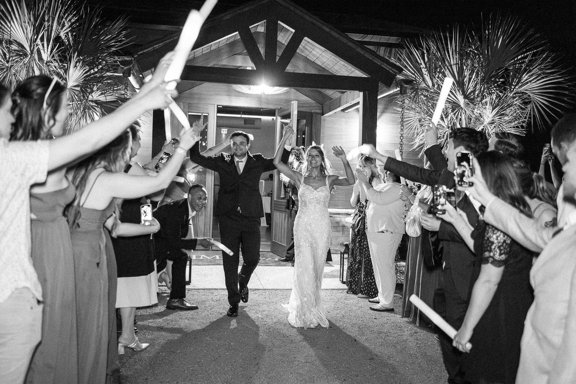 Guests line a decorated walkway with sparklers as a couple walks through a venue entrance at night.