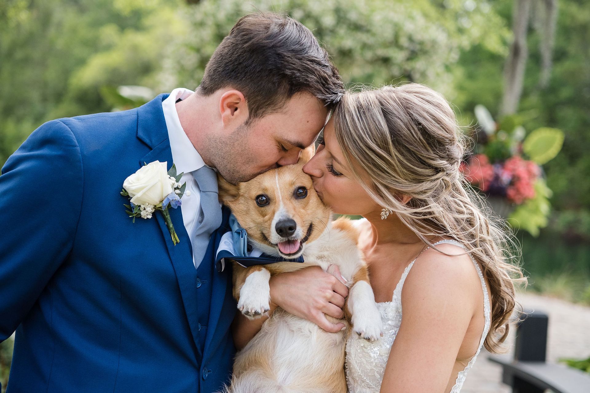 Couple kissing their golden retriever at an outdoor wedding, with the dog wearing a bow tie