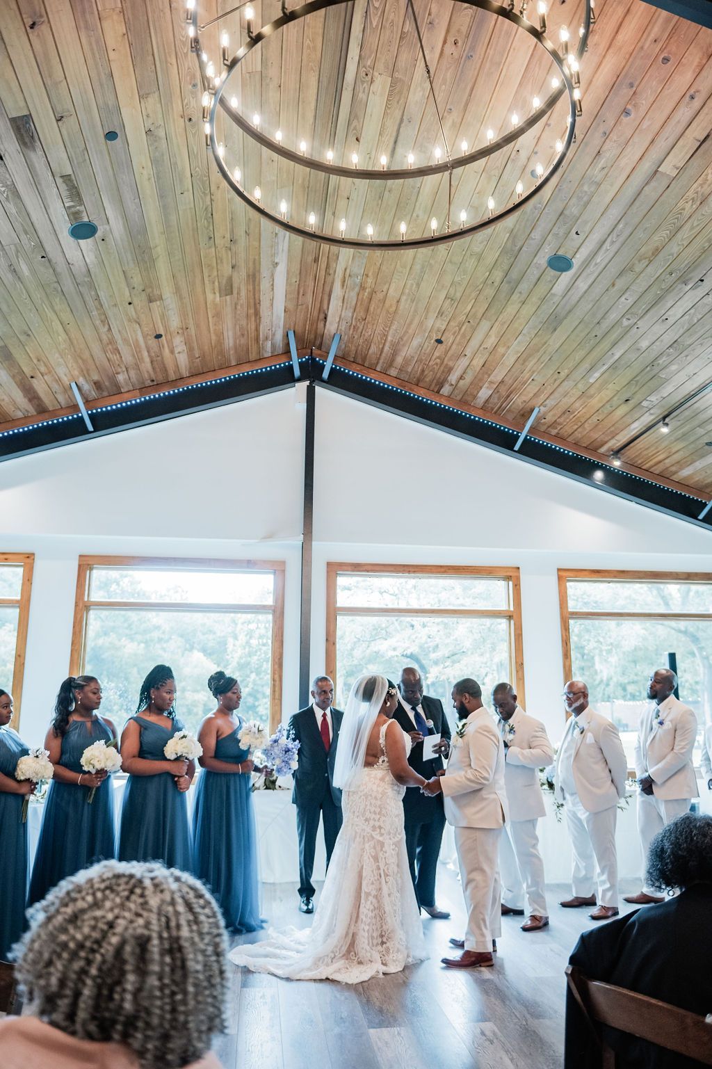 Wedding ceremony in a bright hall with wood ceilings, bride and groom at the altar, guests standing nearby