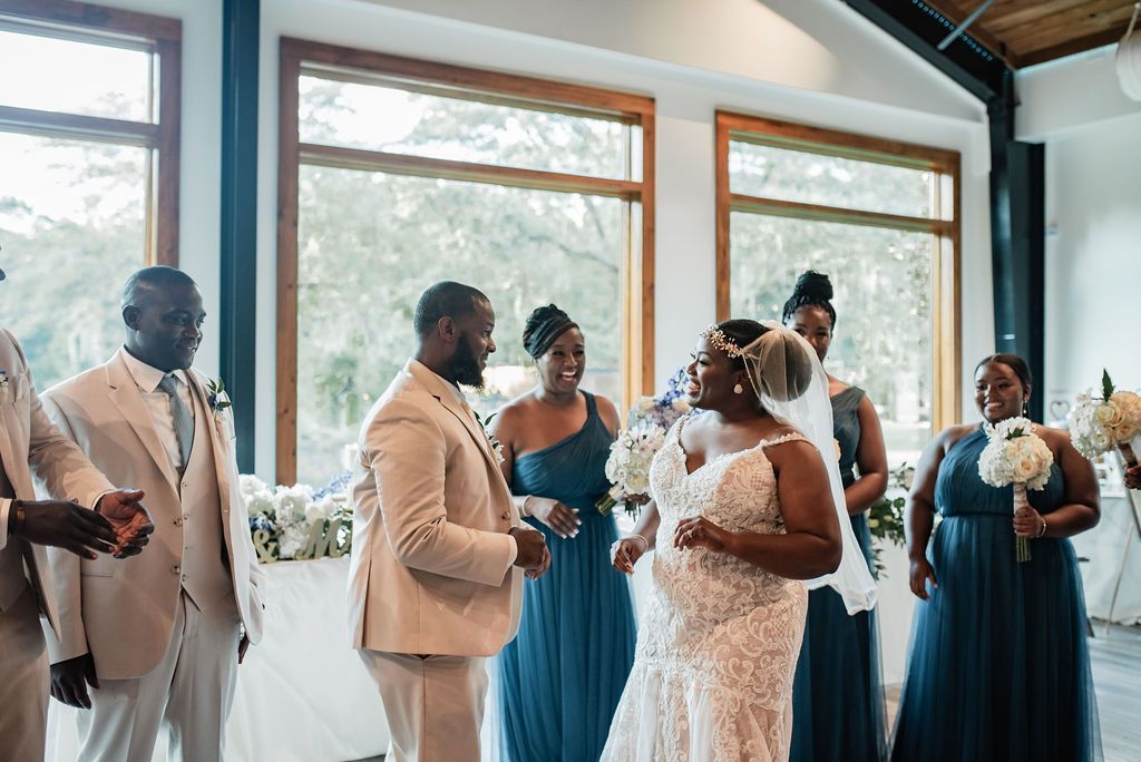 Wedding party standing in a bright room, with the bride and groom facing each other during the ceremony.