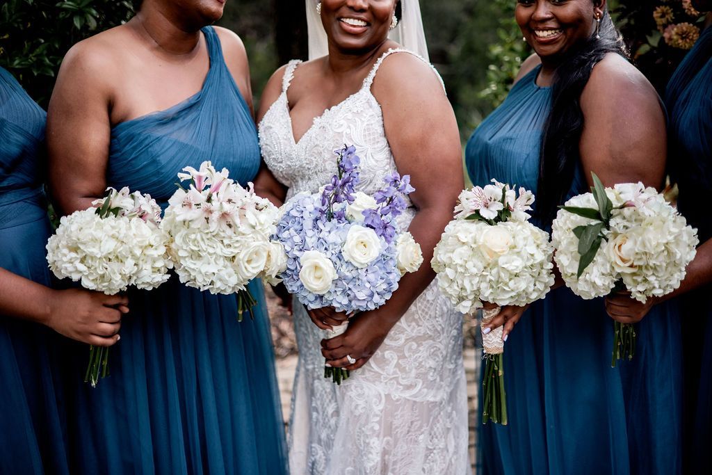 Three bridesmaids in blue dresses holding white and lavender bouquets outdoors