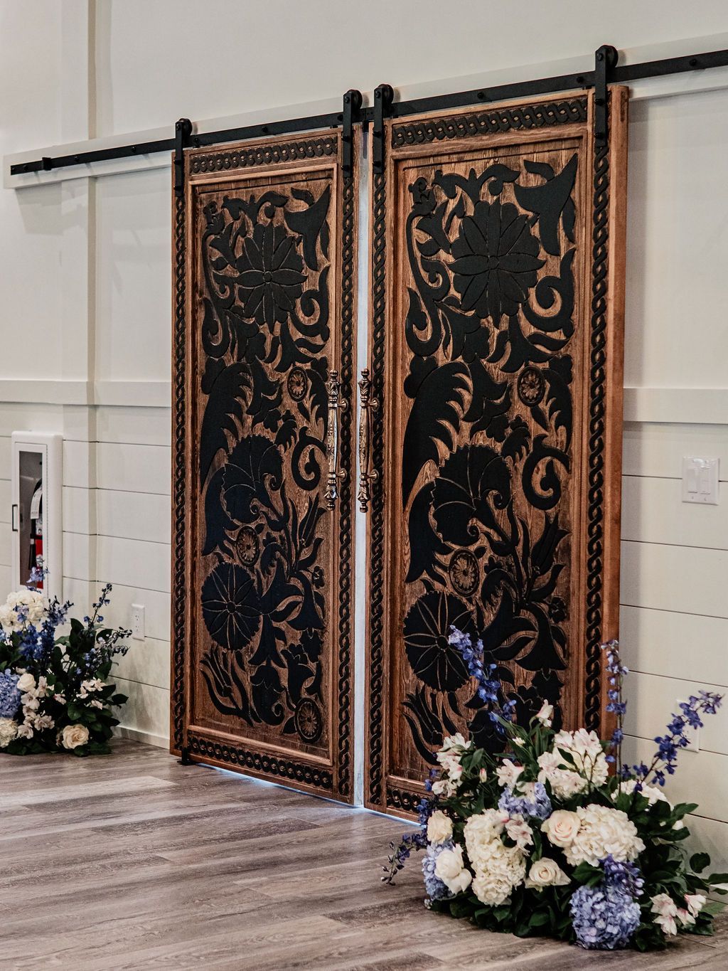 Ornate black and gold double doors with floral arrangements in a bright indoor venue