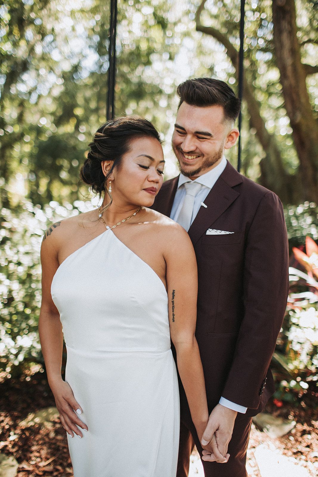 Couple in wedding attire standing outdoors, smiling at each other in a garden.