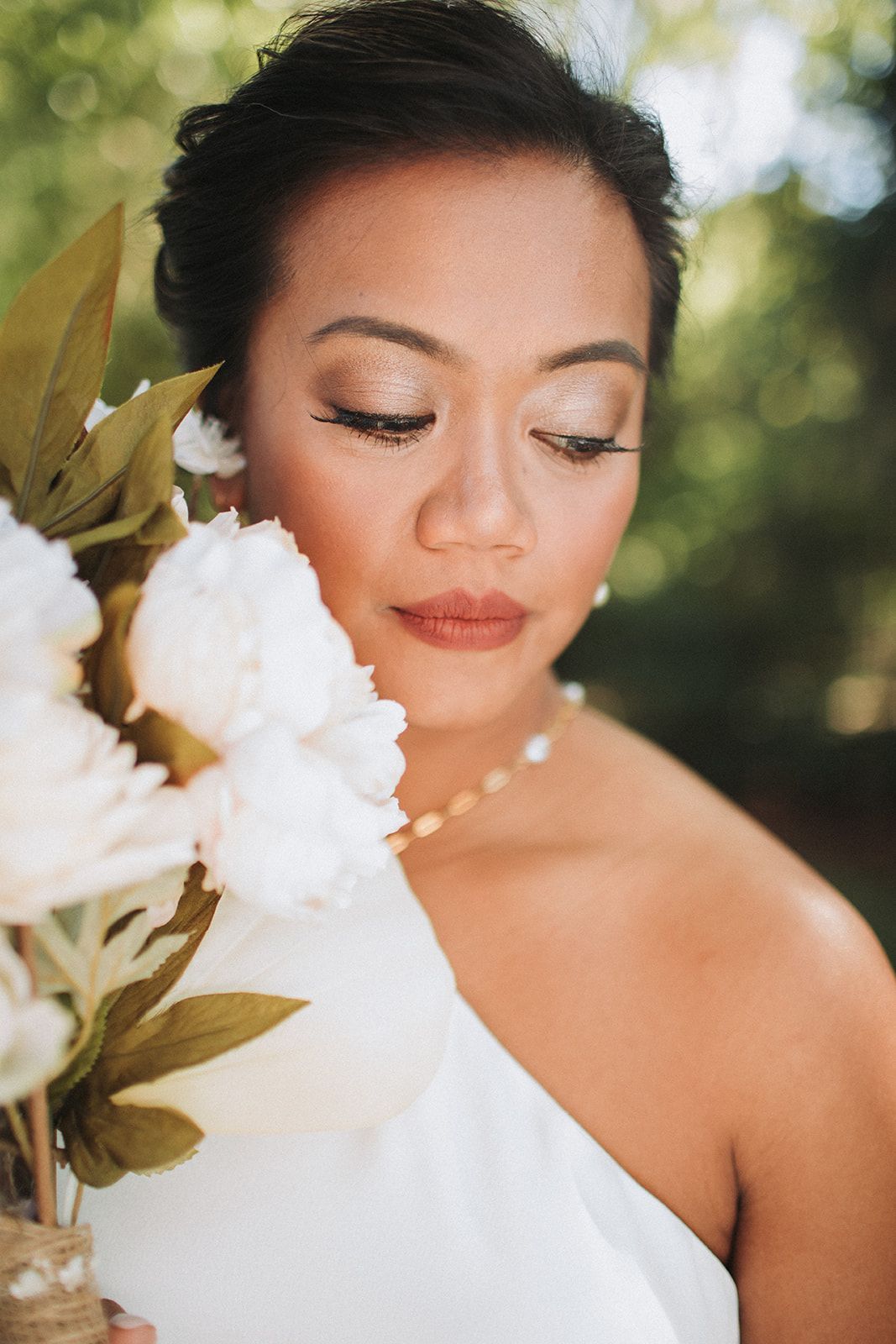 Woman in a white dress with flowers, eyes closed, against a soft green background.