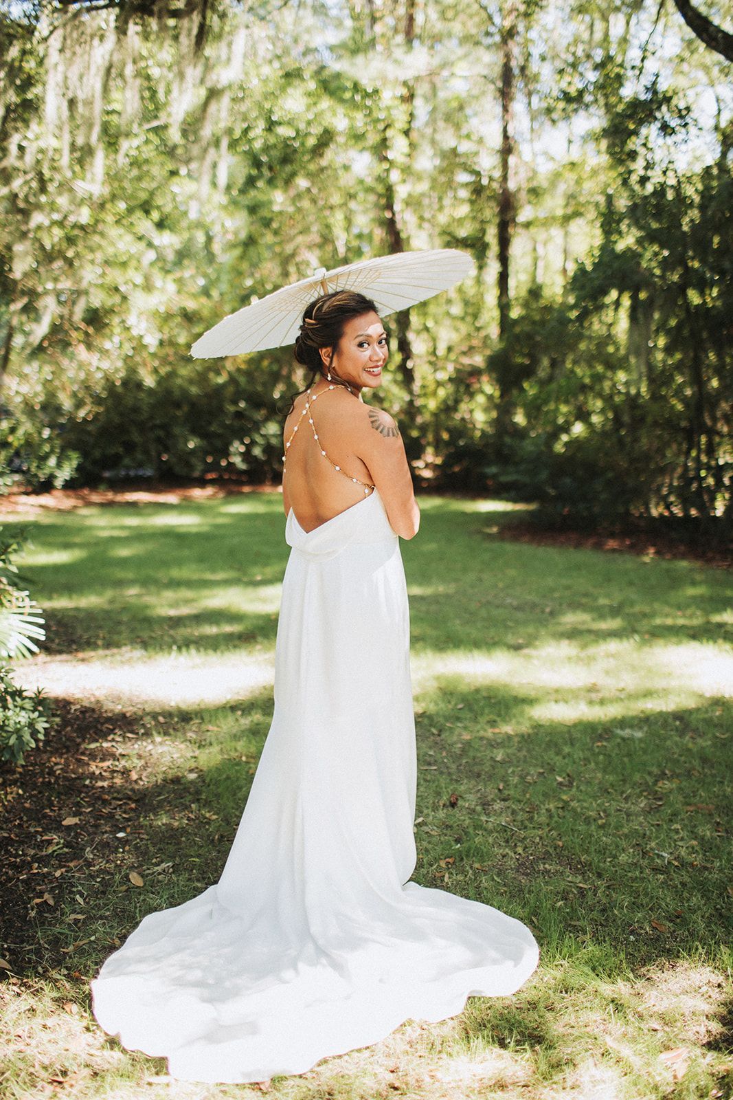 Woman in a white dress holding a parasol in a sunlit garden walkway