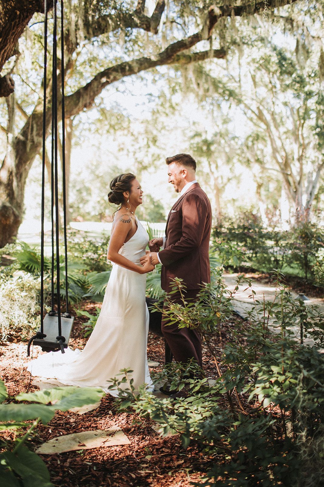 Bride and groom standing together in a sunlit garden under leafy trees