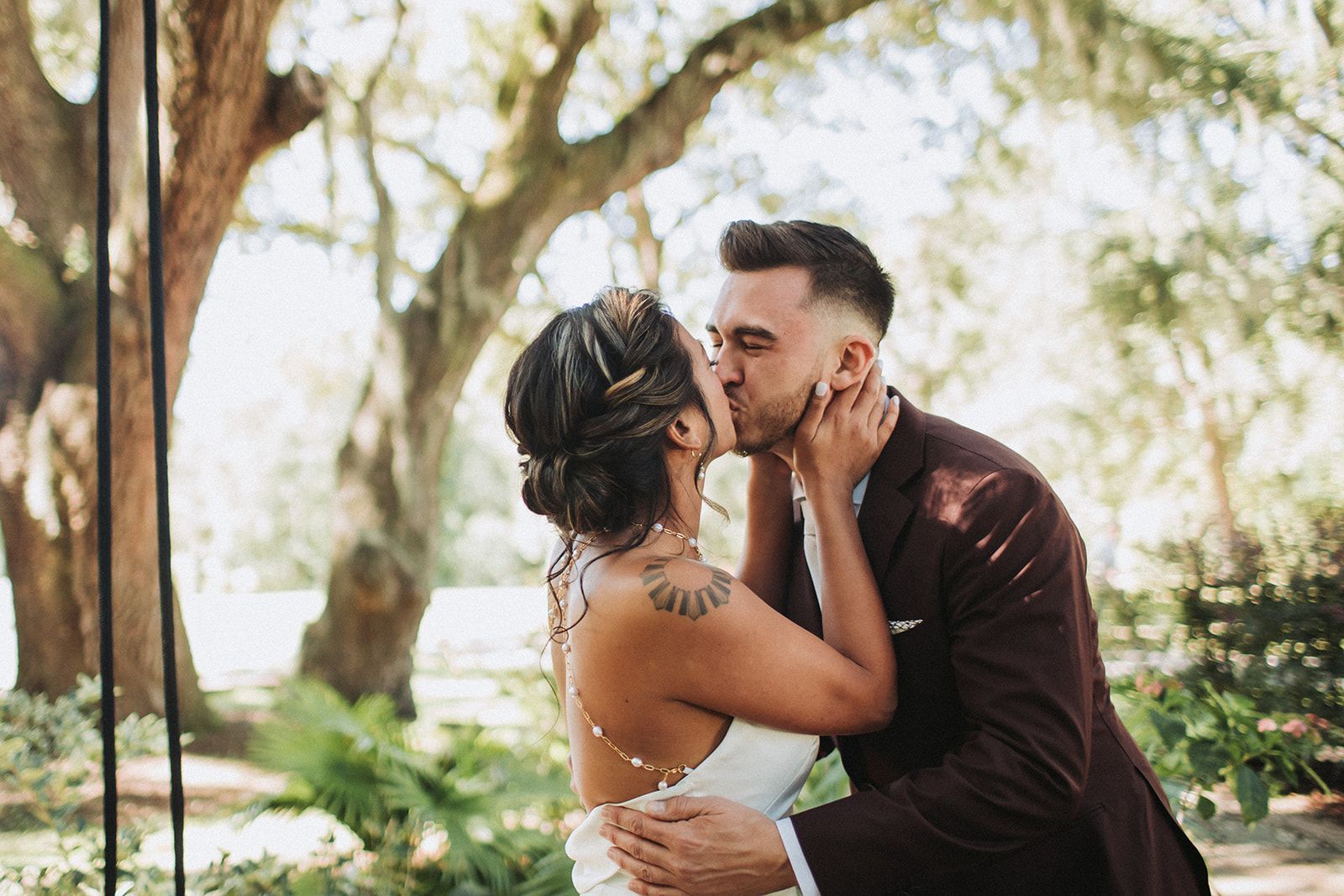 Couple kissing outdoors under trees, with the man holding the woman in a garden setting
