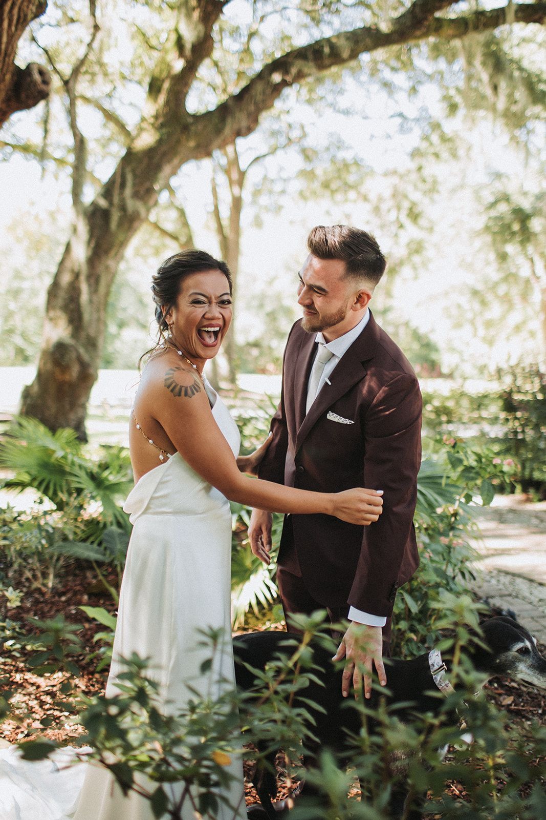 Smiling couple in formal attire holding hands in a leafy garden outdoors