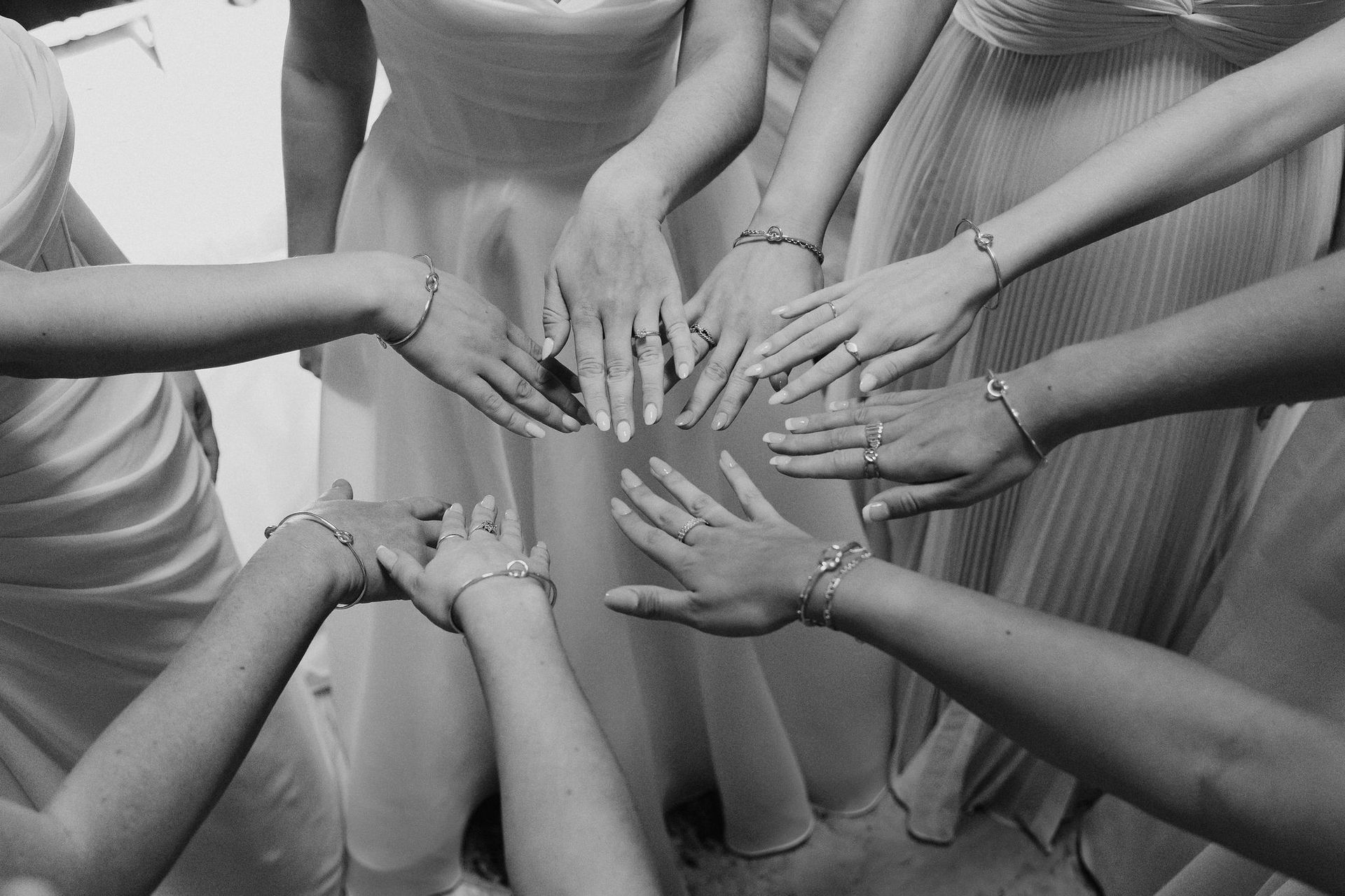 Hands of several people stacked together in a team huddle, black-and-white.