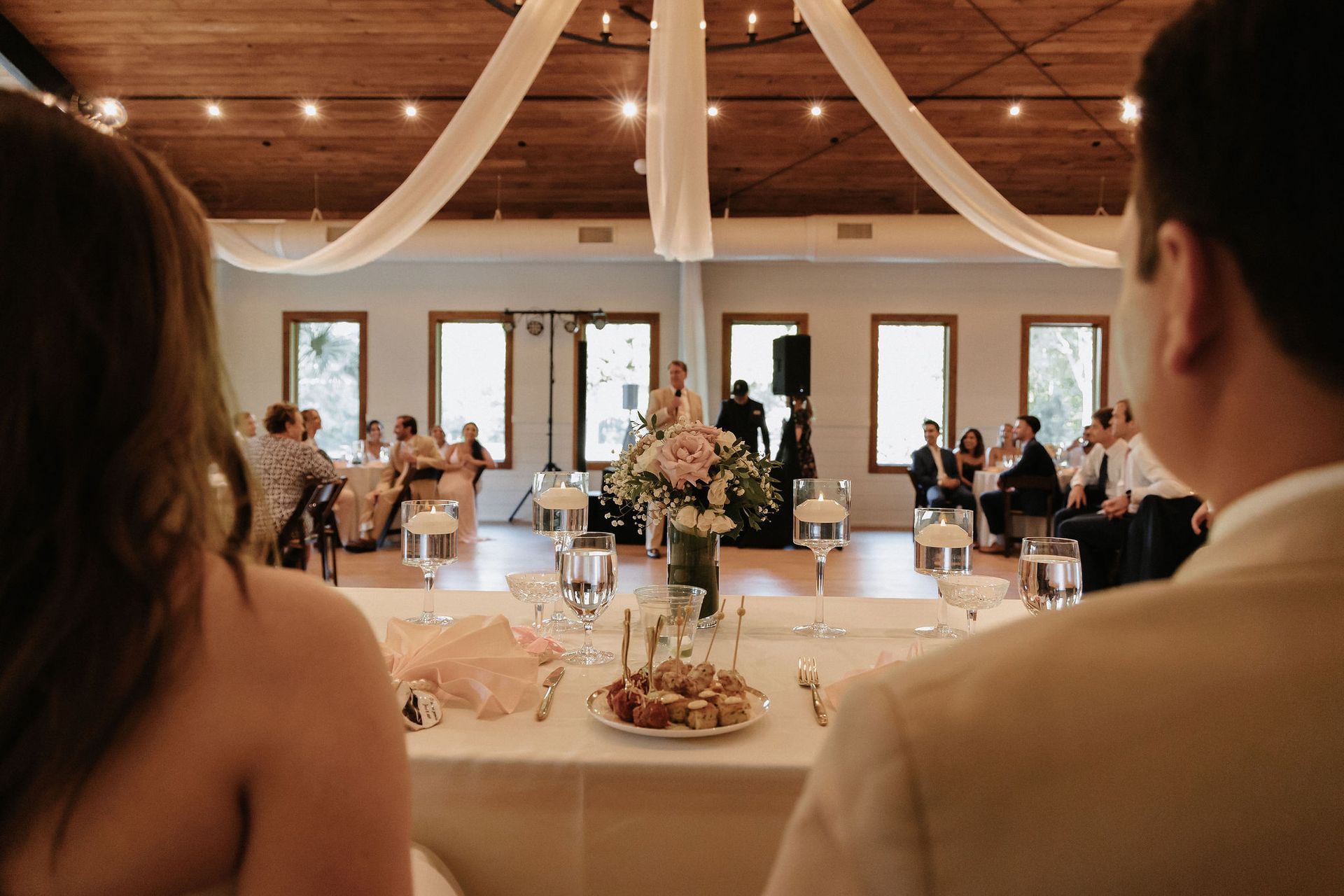 Wedding reception hall viewed from the couple’s table, with guests seated at decorated tables.