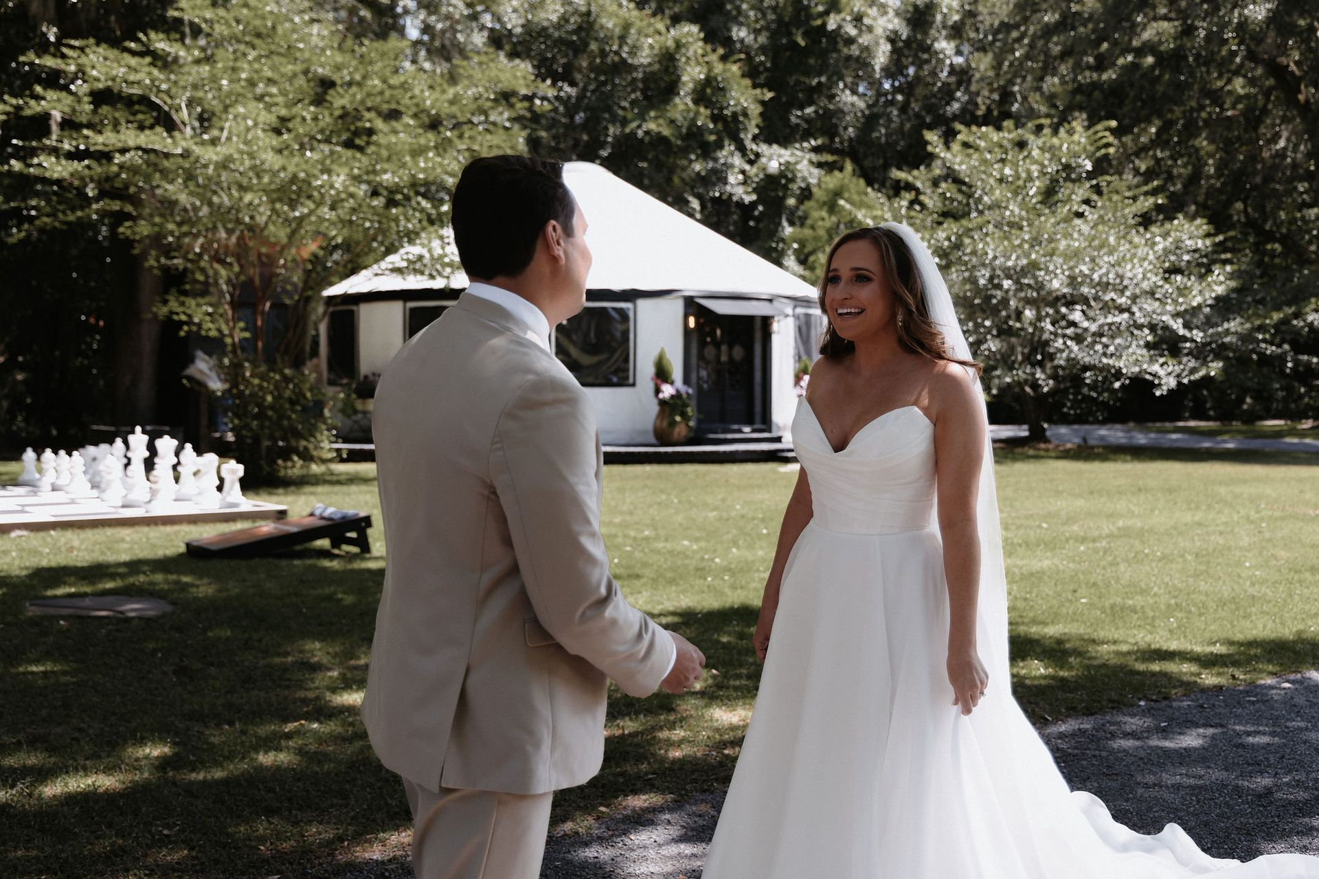 Couple in wedding attire standing outdoors near a white tent, smiling at each other.