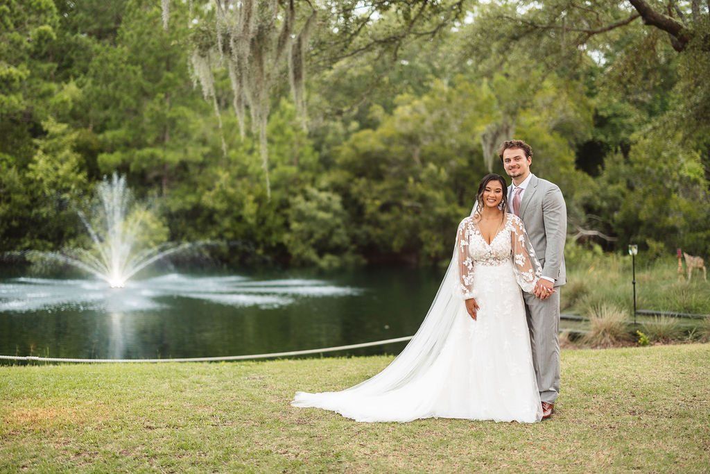 Wedding couple in white and gray standing on grass by a fountain in a park