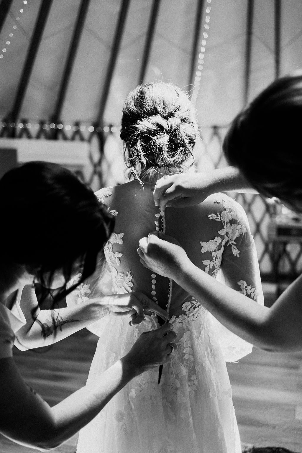 Bride surrounded by attendants adjusting her dress and veil in a sunlit room