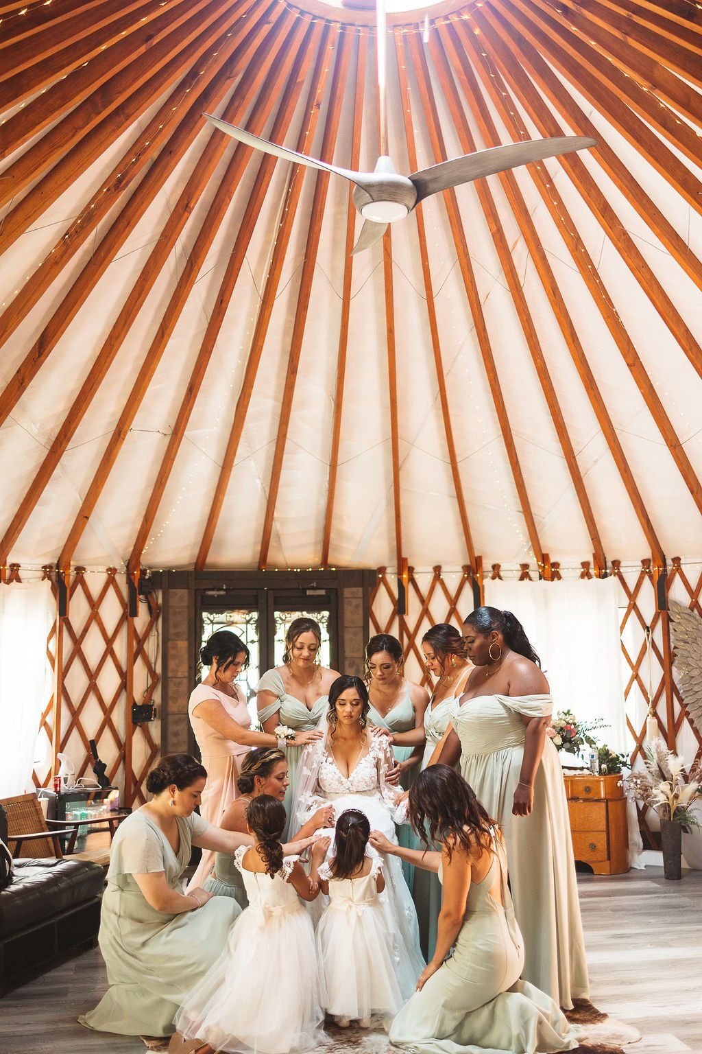 Wedding party gathered inside a circular yurt with striped ceiling and open floor, posing around the bride.