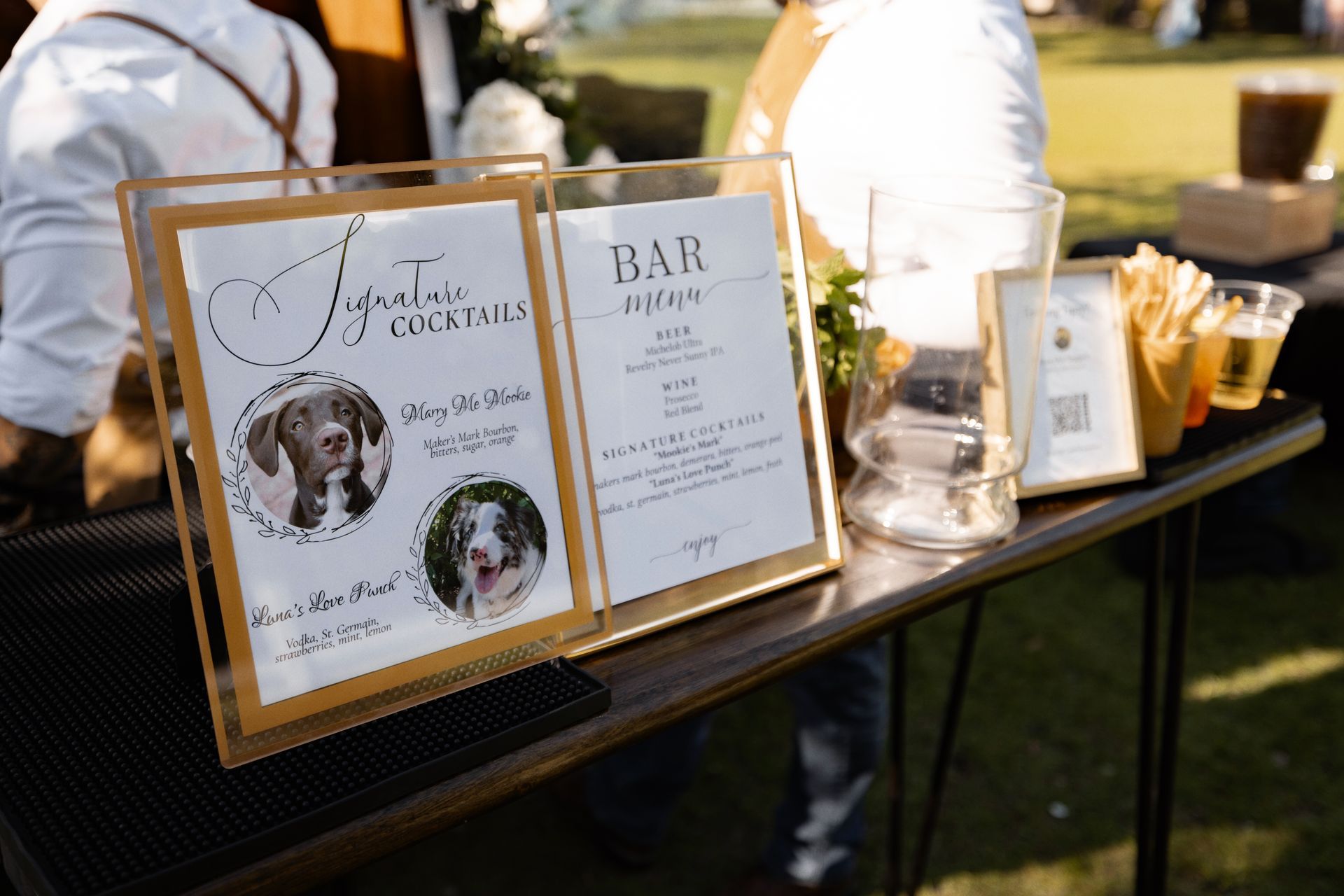 Wedding welcome table with gold-framed signs, candles, and a guest book outdoors
