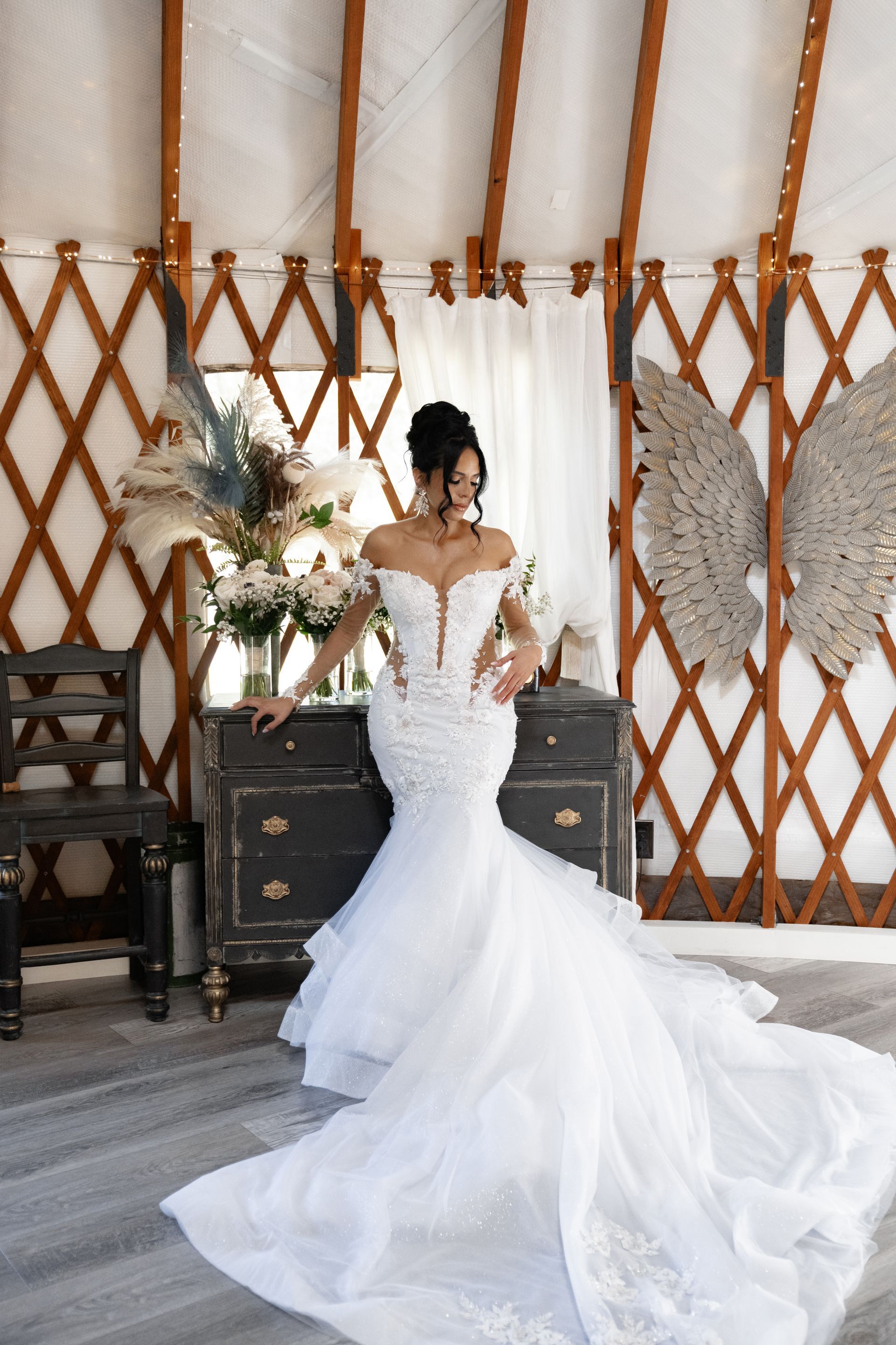 Bride in a white mermaid gown standing in a rustic tent with wooden lattice decor and flowers