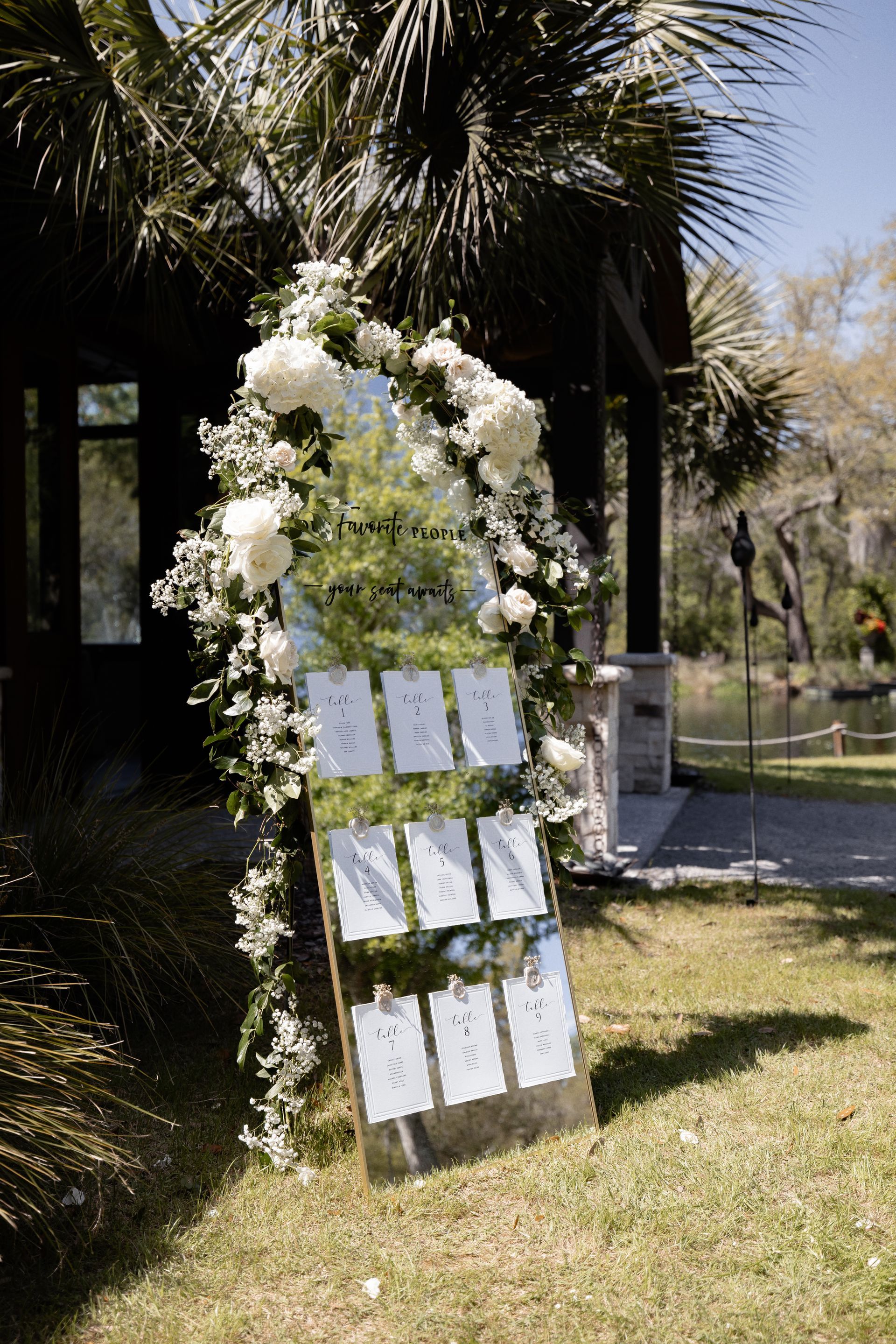White flower arch with hanging cards on a lawn beside palm trees and a garden path