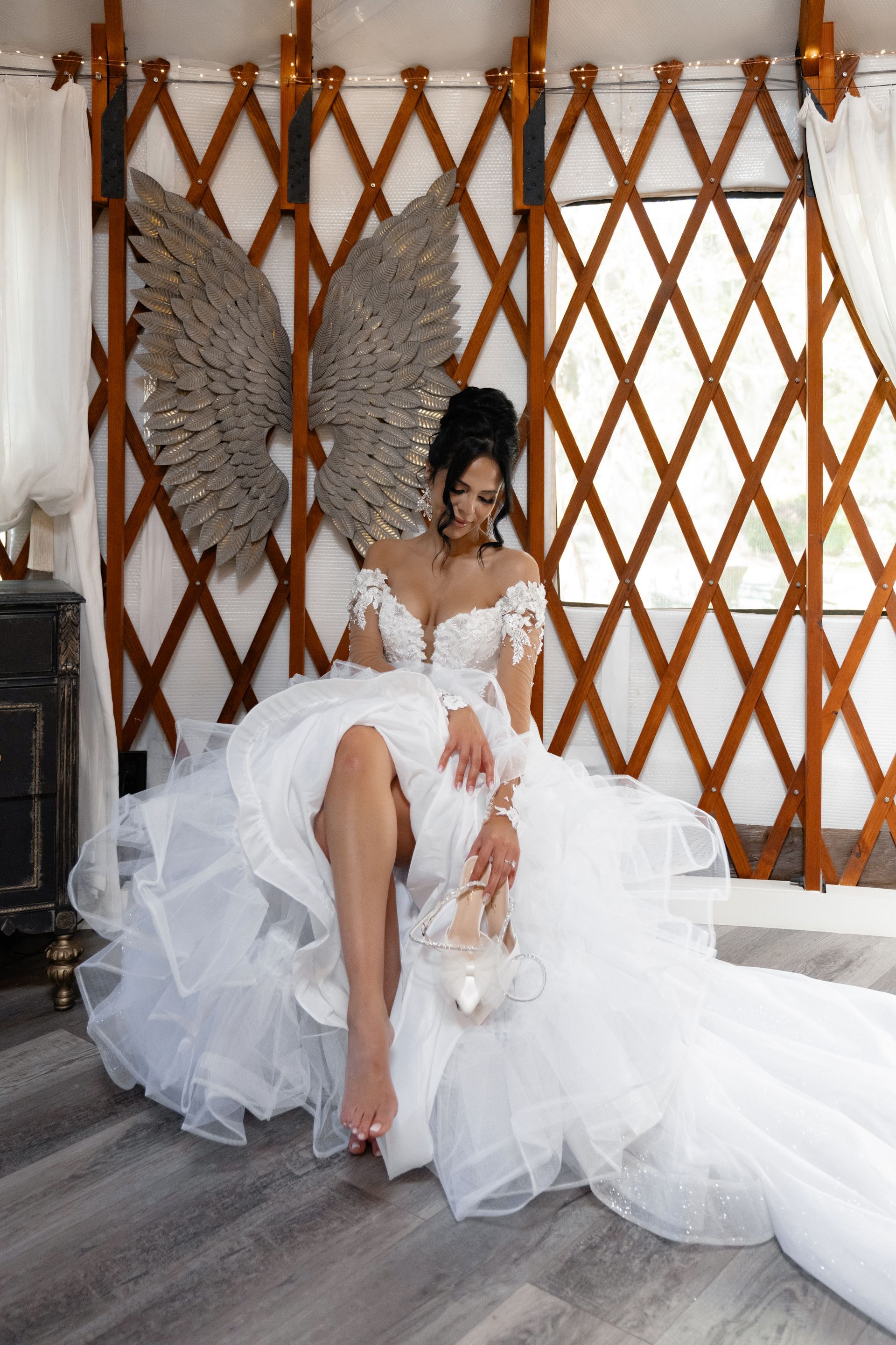 Person in a voluminous white dress seated indoors against a wooden lattice backdrop