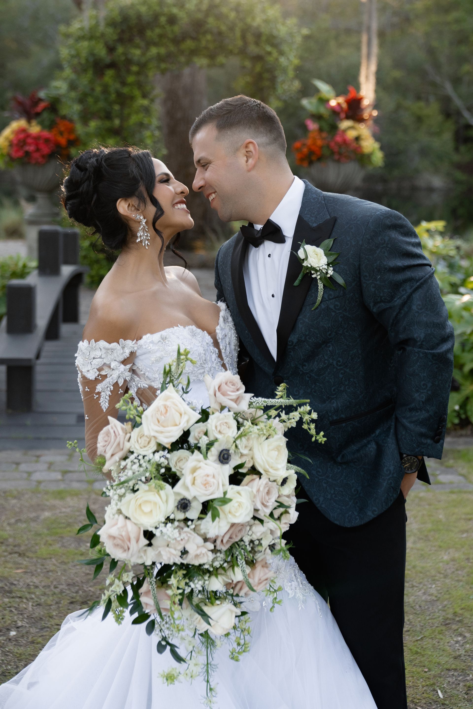 Bride and groom smiling at each other outdoors, holding a large white bouquet at their wedding