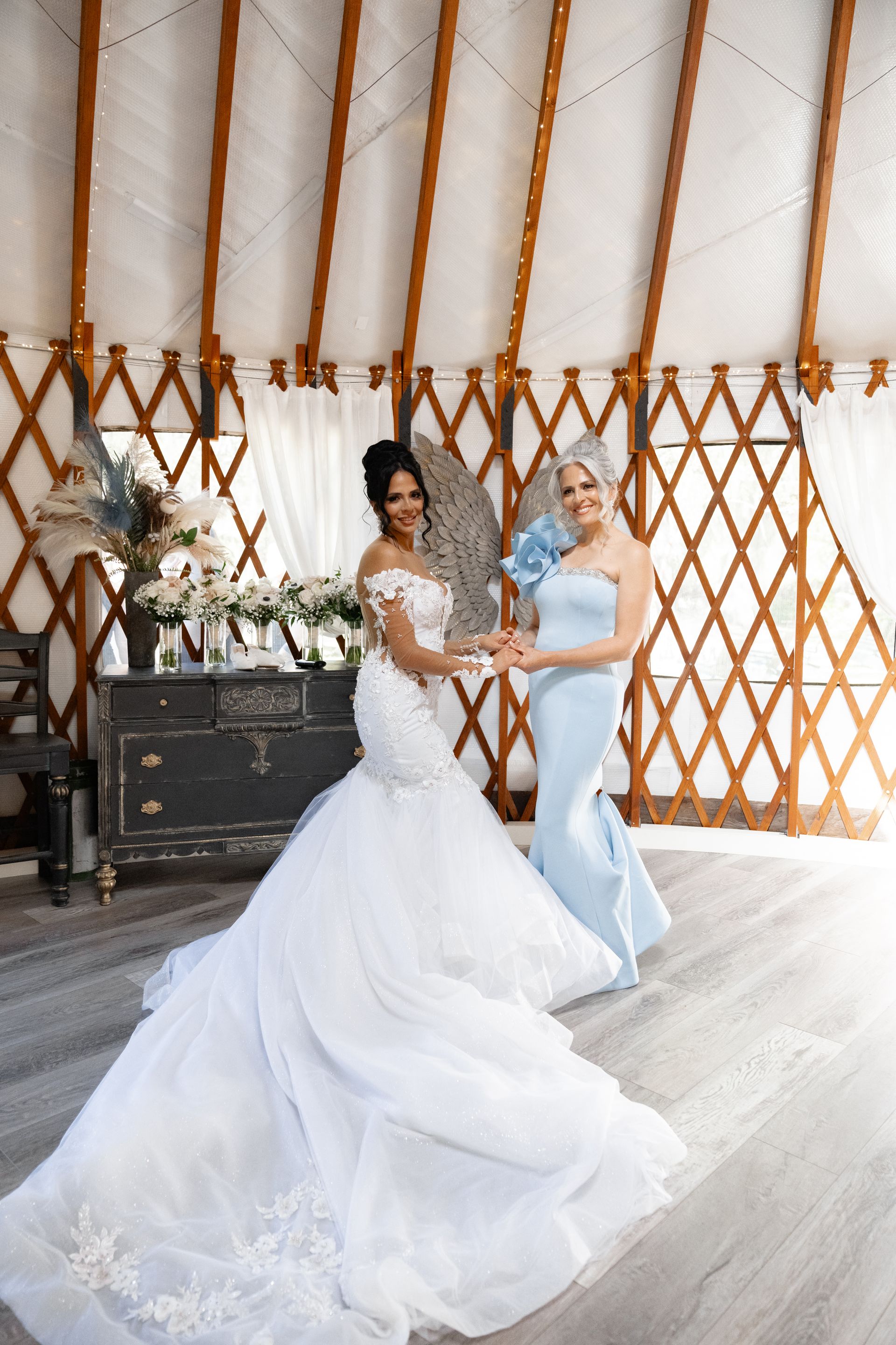 Two women in white and light blue wedding dresses standing in a yurt-style venue