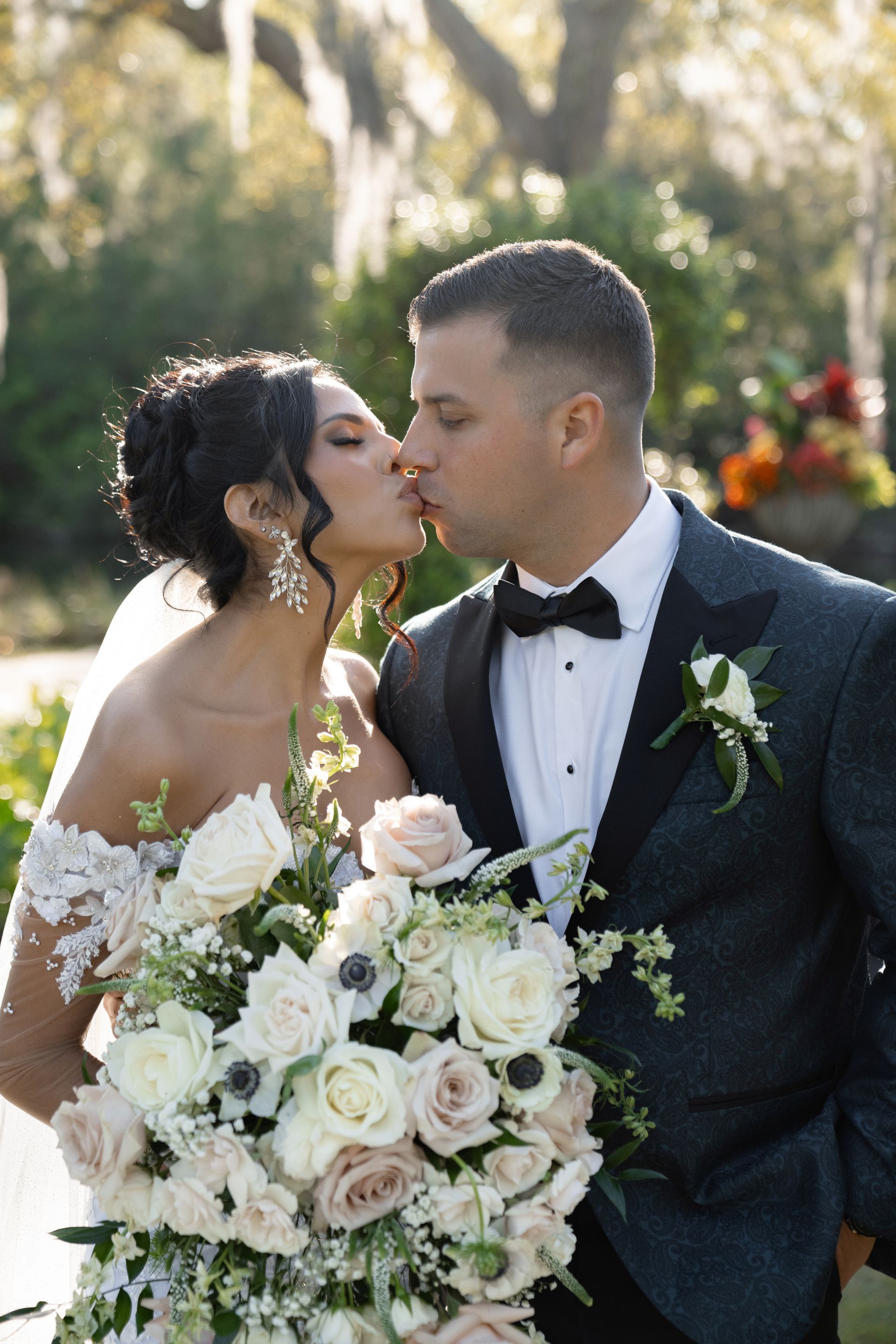 Wedding couple kissing, bride holding white rose bouquet outdoors in sunlight