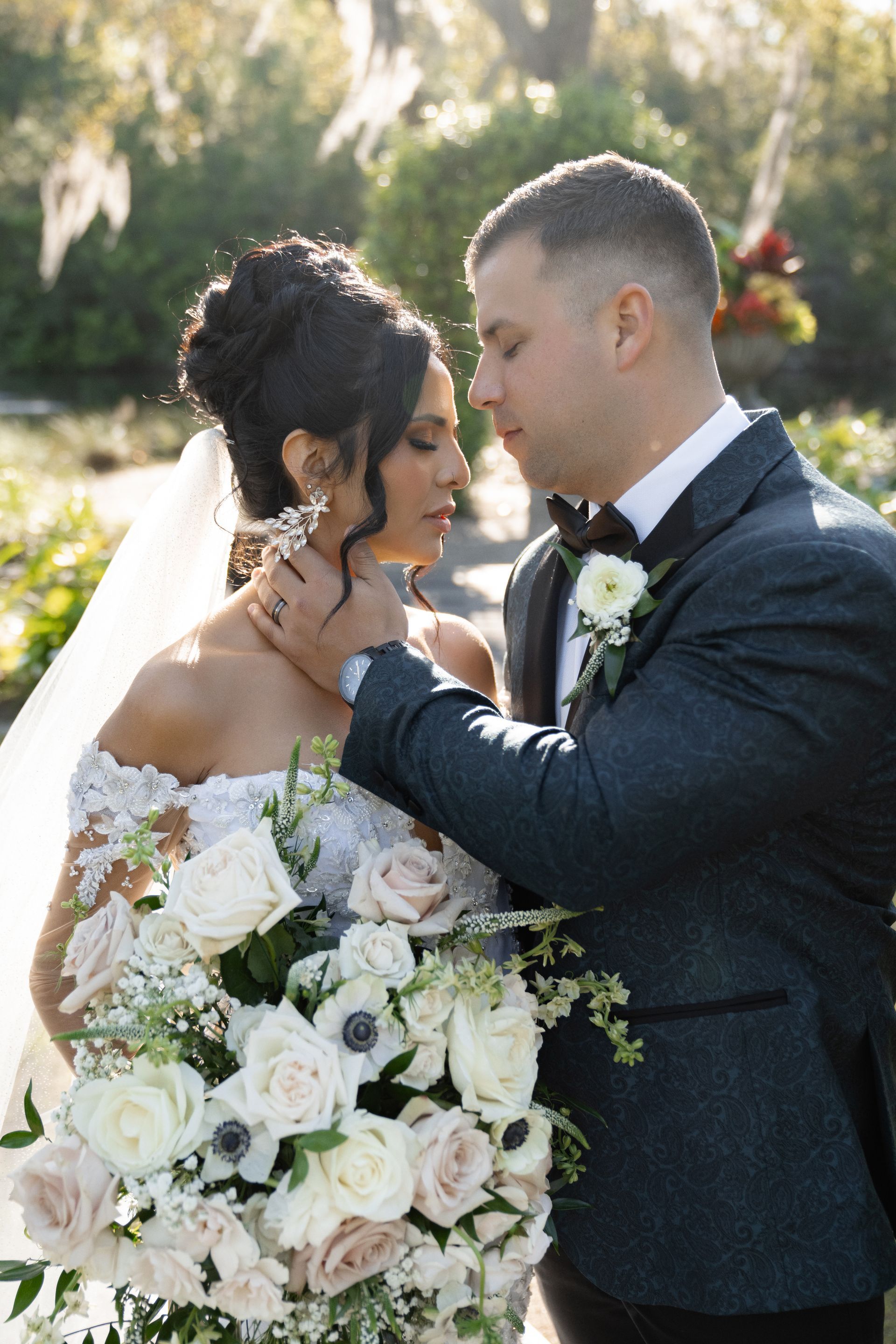 Bride and groom sharing a tender moment outdoors, holding a large white rose bouquet