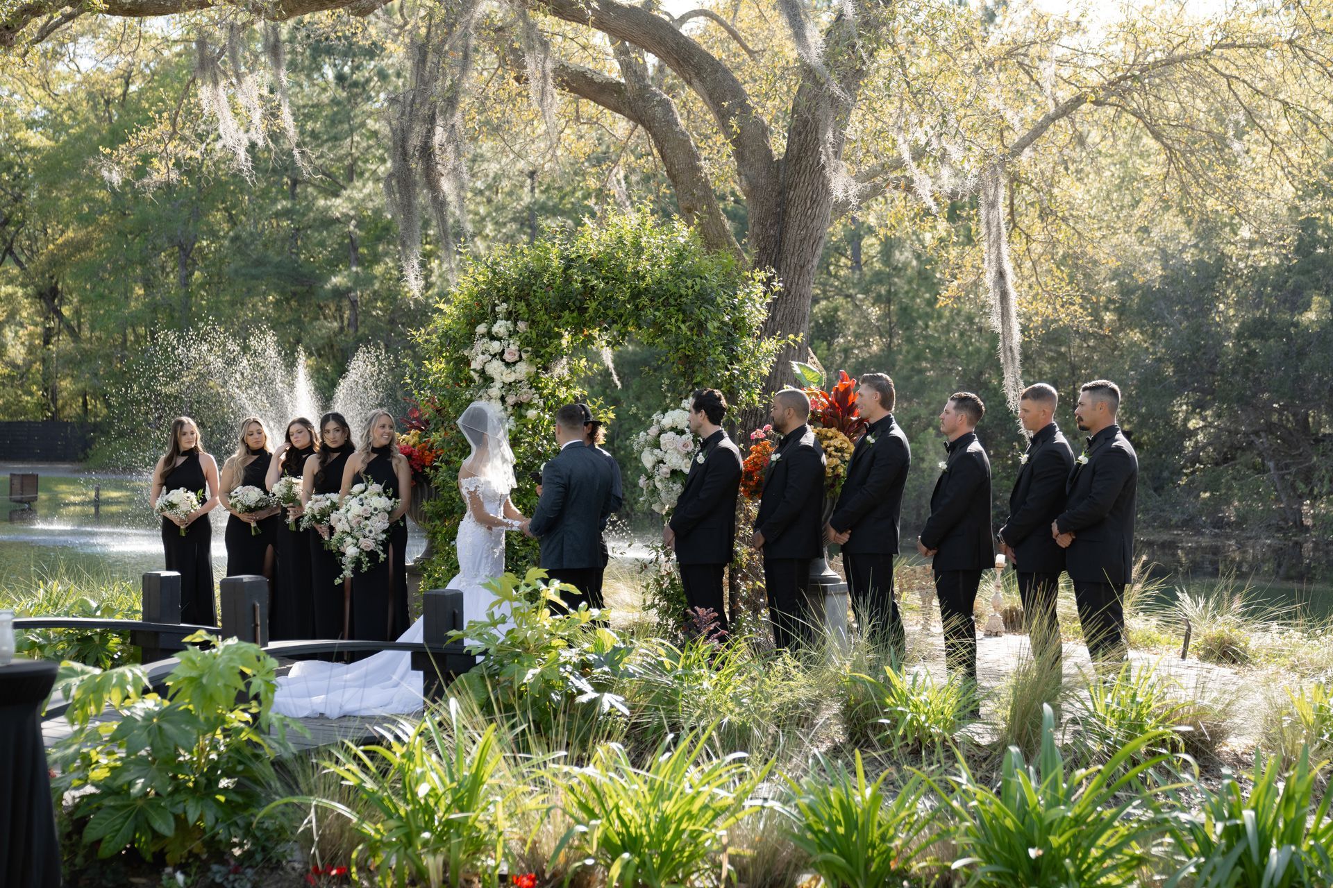 Mourners gathered outdoors around a flower-covered casket at a memorial service under trees.