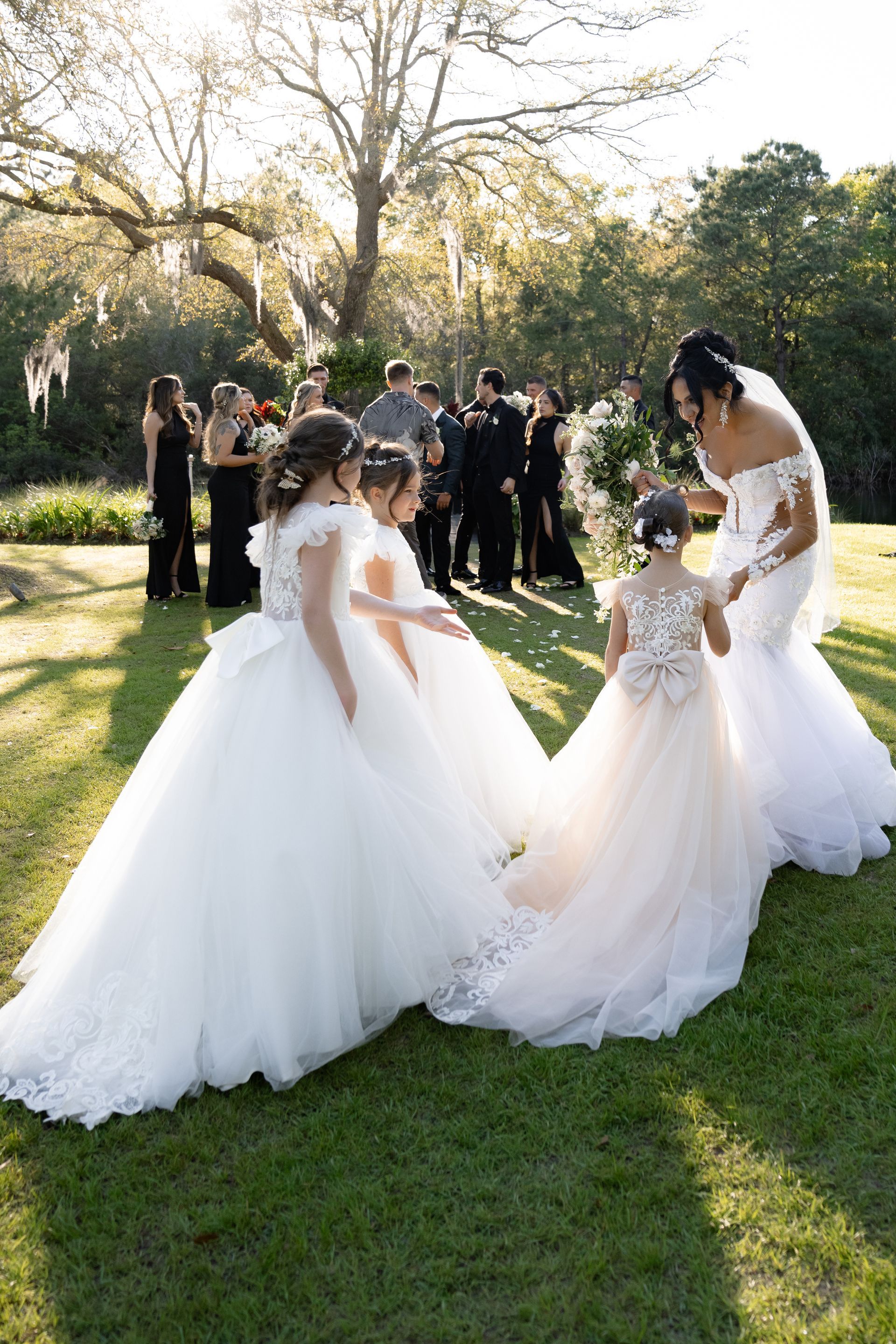 Three brides in white gowns sharing a veil at an outdoor wedding ceremony