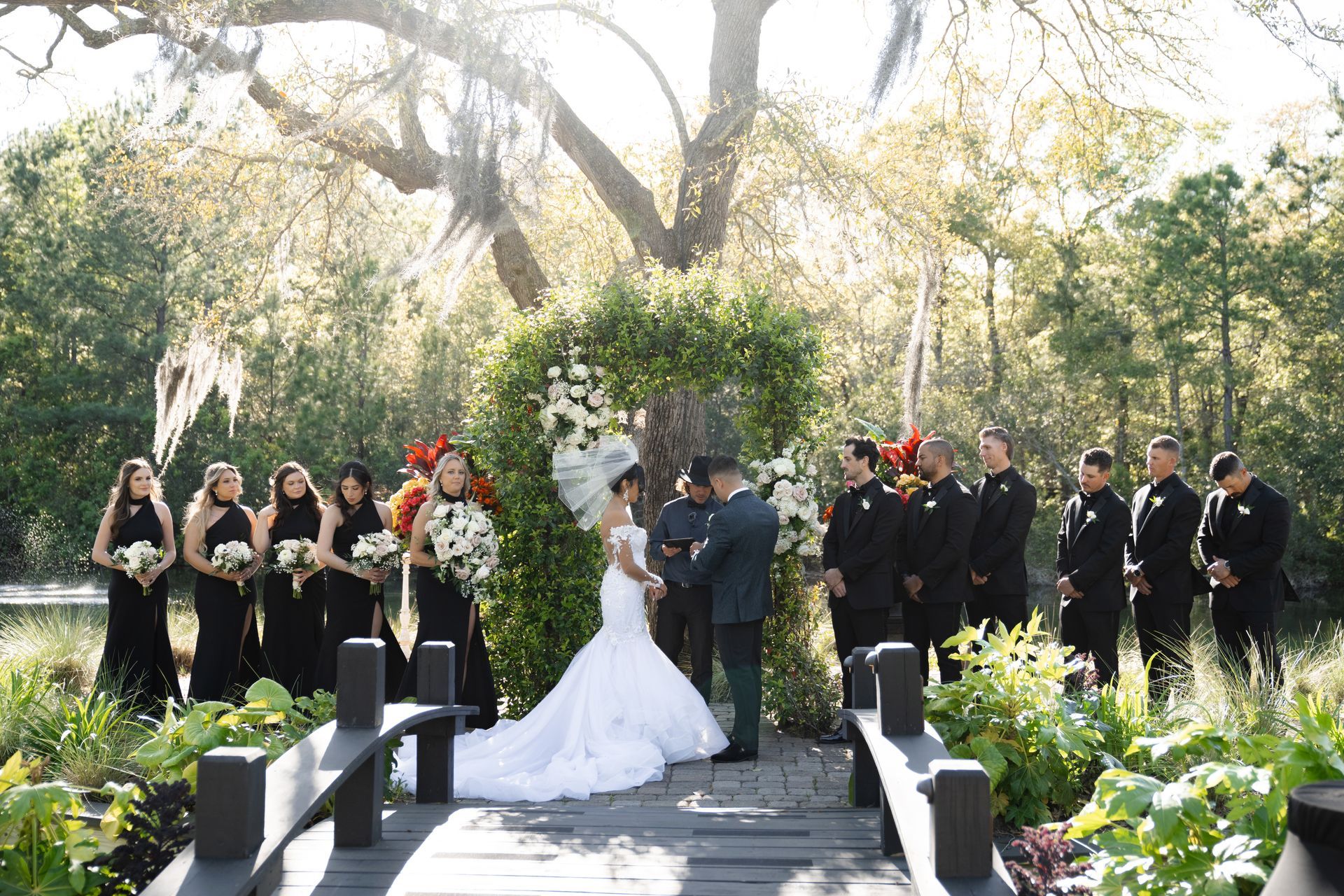 Outdoor wedding ceremony with bride and groom exchanging vows in a garden, surrounded by attendants.