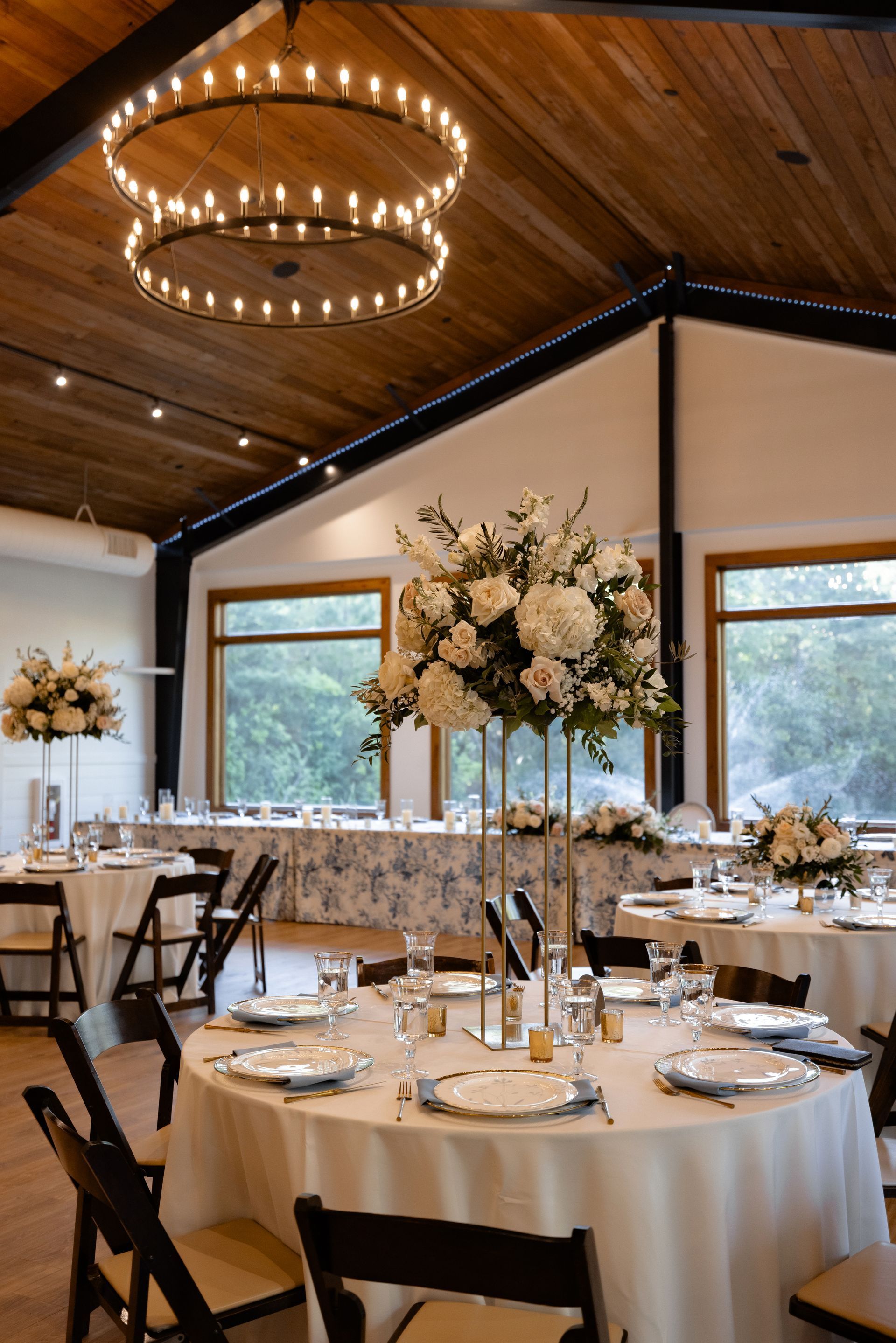 Elegant banquet room with round tables, white florals, and warm chandelier lighting under a wood ceiling