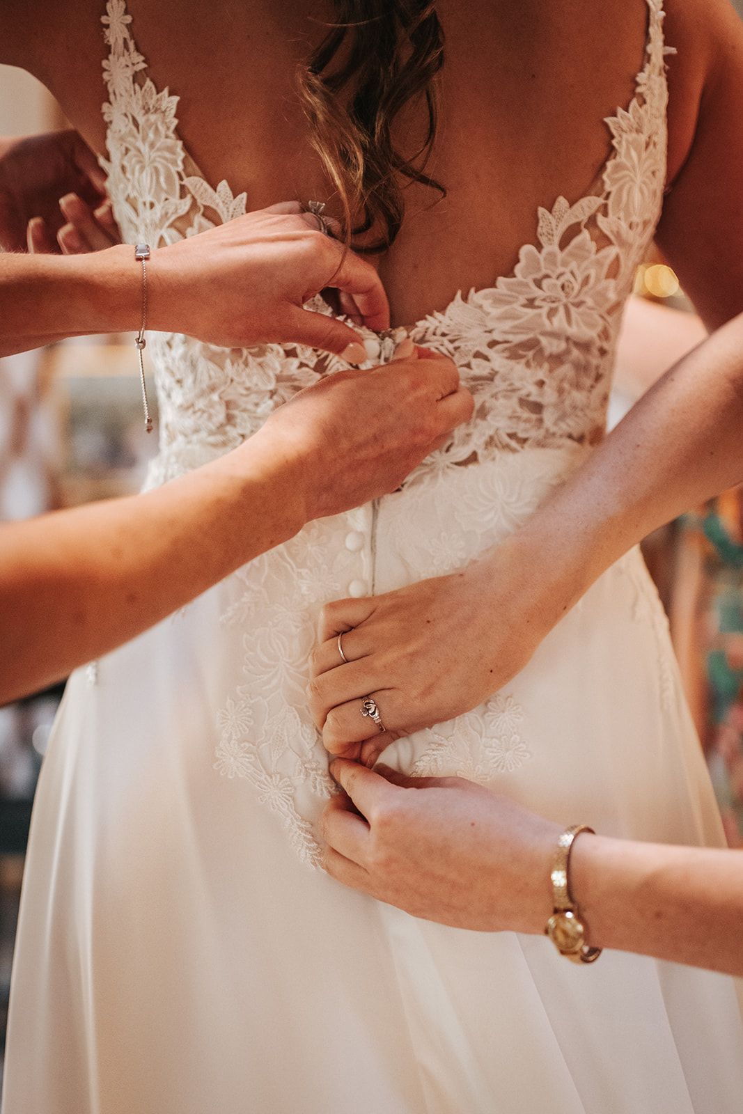 Hands fasten the back of a white lace wedding dress.