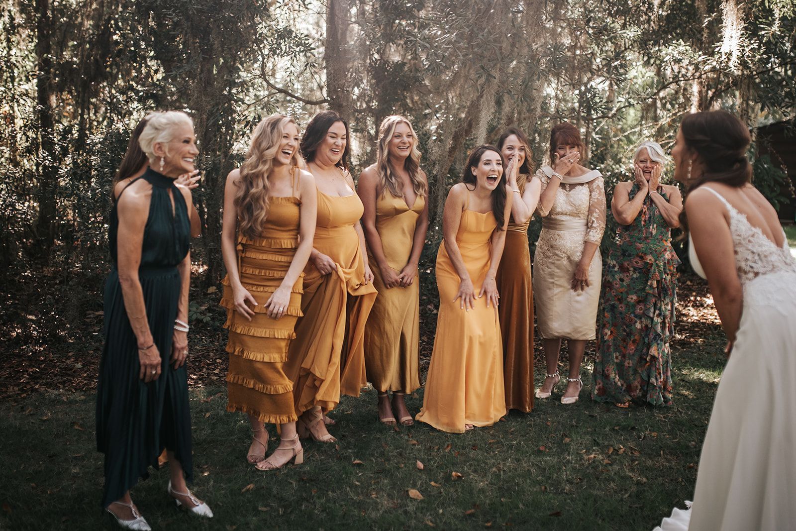 Group of people in yellow dresses and rustic clothing gathered outdoors in a garden, facing a woman in white.