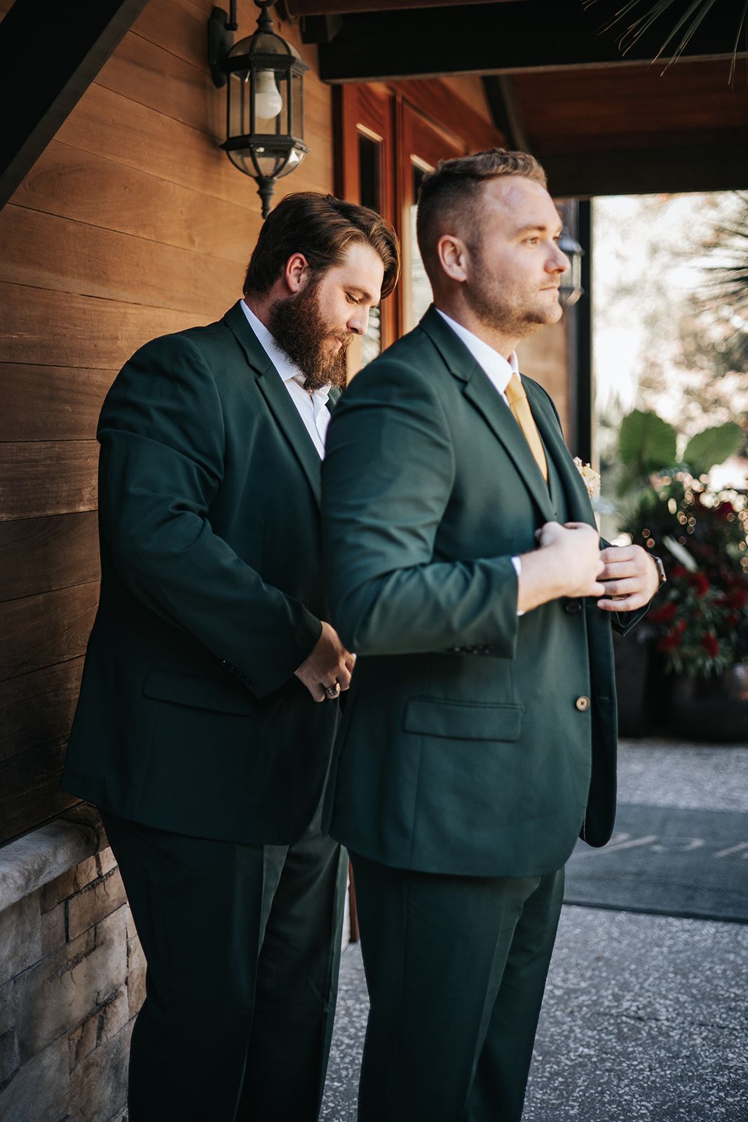 Two men in green suits standing by a brick wall, one looking out through an open doorway outdoors