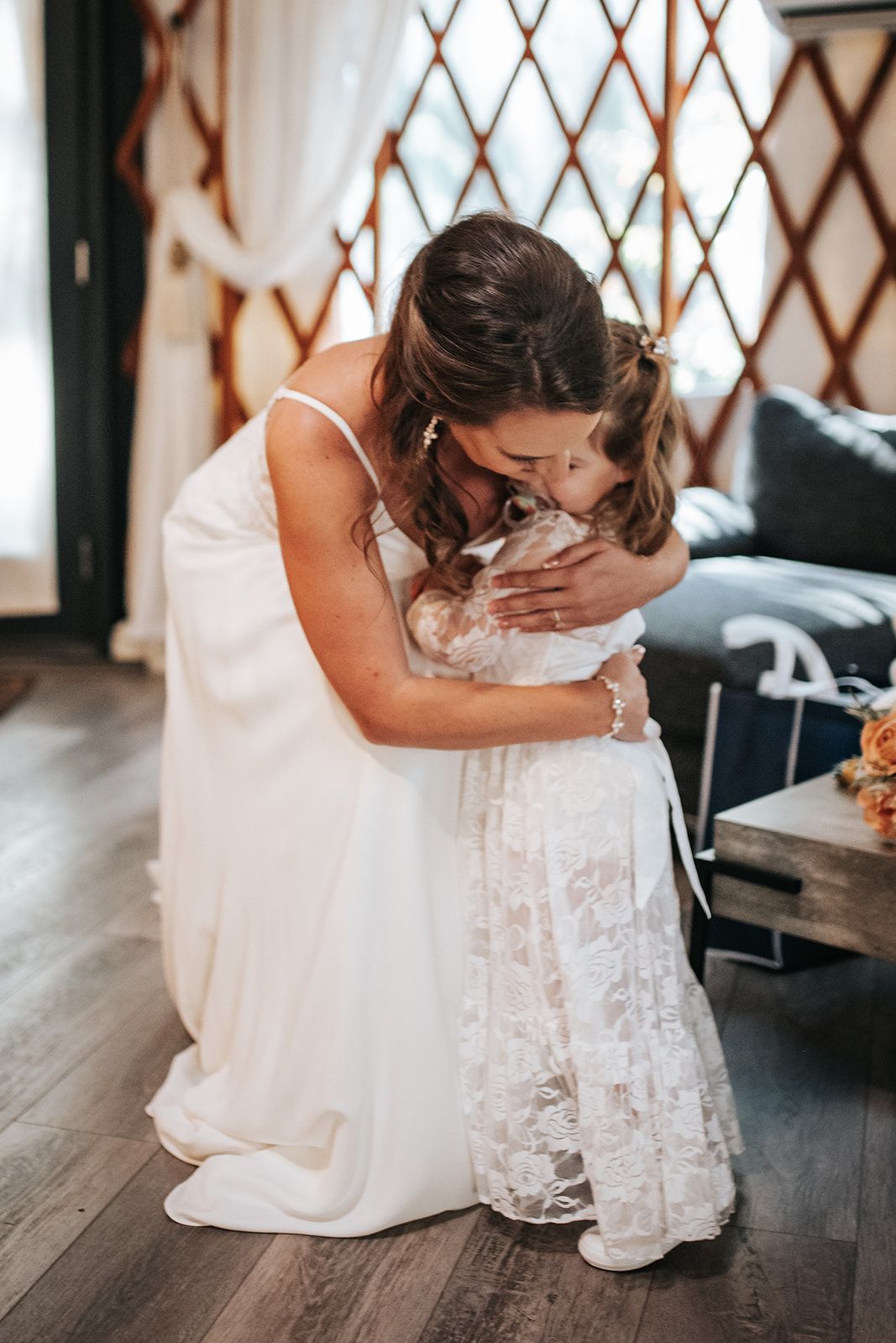 Woman in a white dress hugging a child in a lace dress indoors