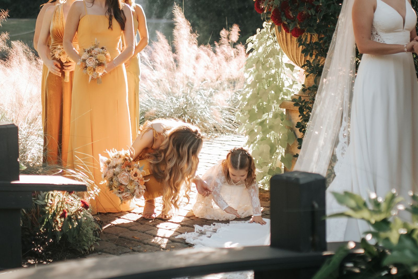 Children and adults playing on a sunlit outdoor stage with flowers and sheer white drapes