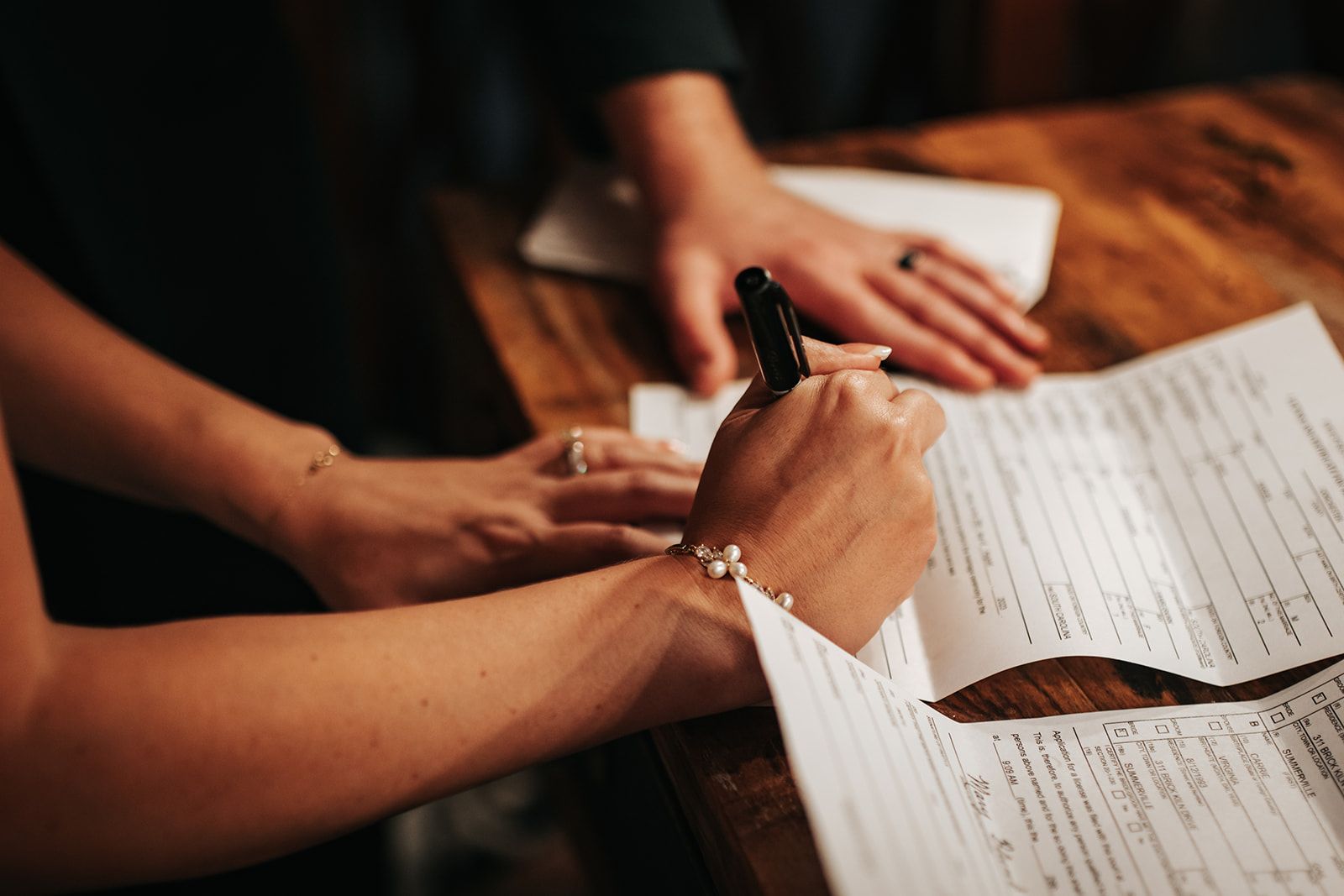 Hands reviewing printed documents at a wooden table, one person writing with a pen.