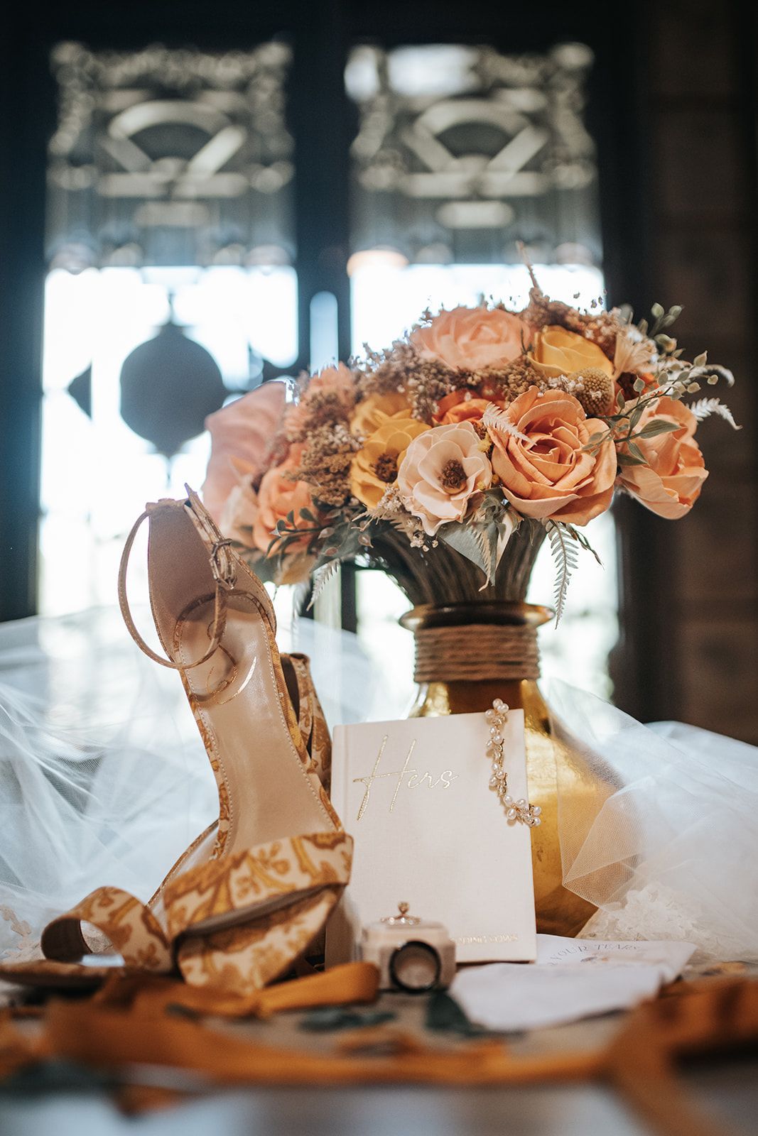 Blush floral bridal bouquet with champagne heels and ring box on a table in a softly lit room