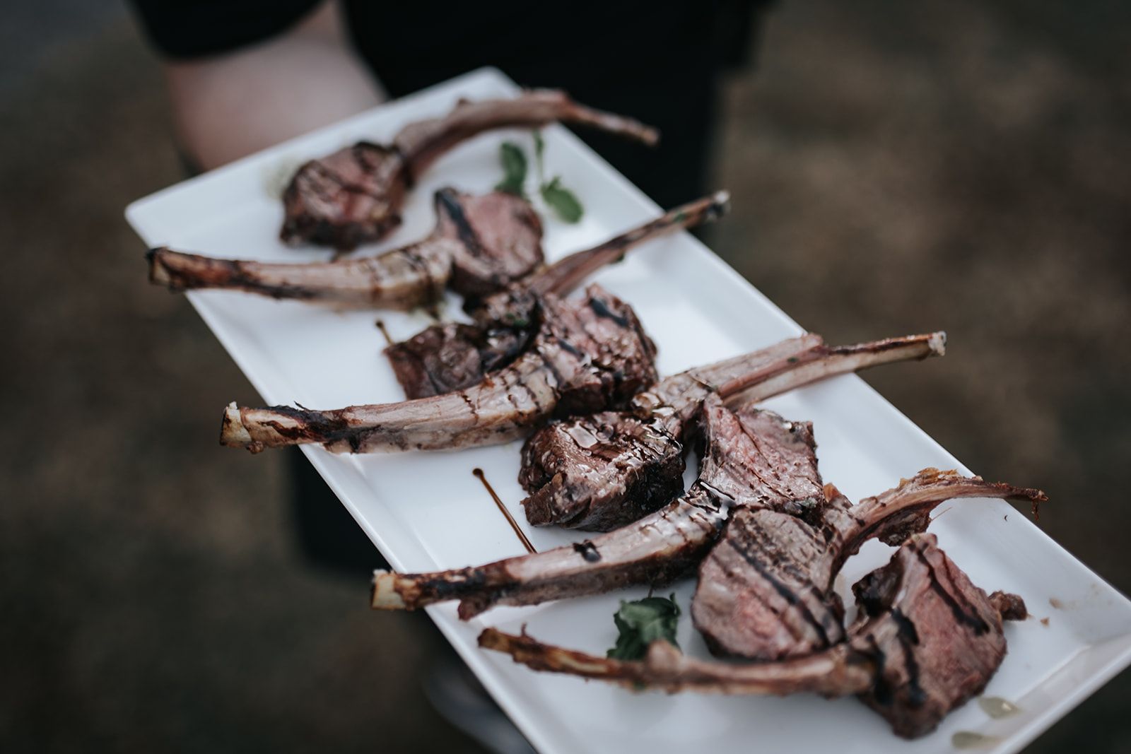 Plated grilled lamb chops with herbs on white rectangular dishes at a buffet