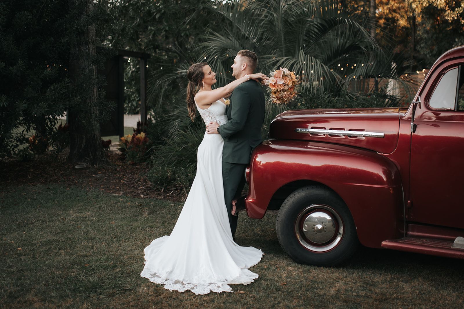 Couple embracing beside a vintage red truck in a garden setting
