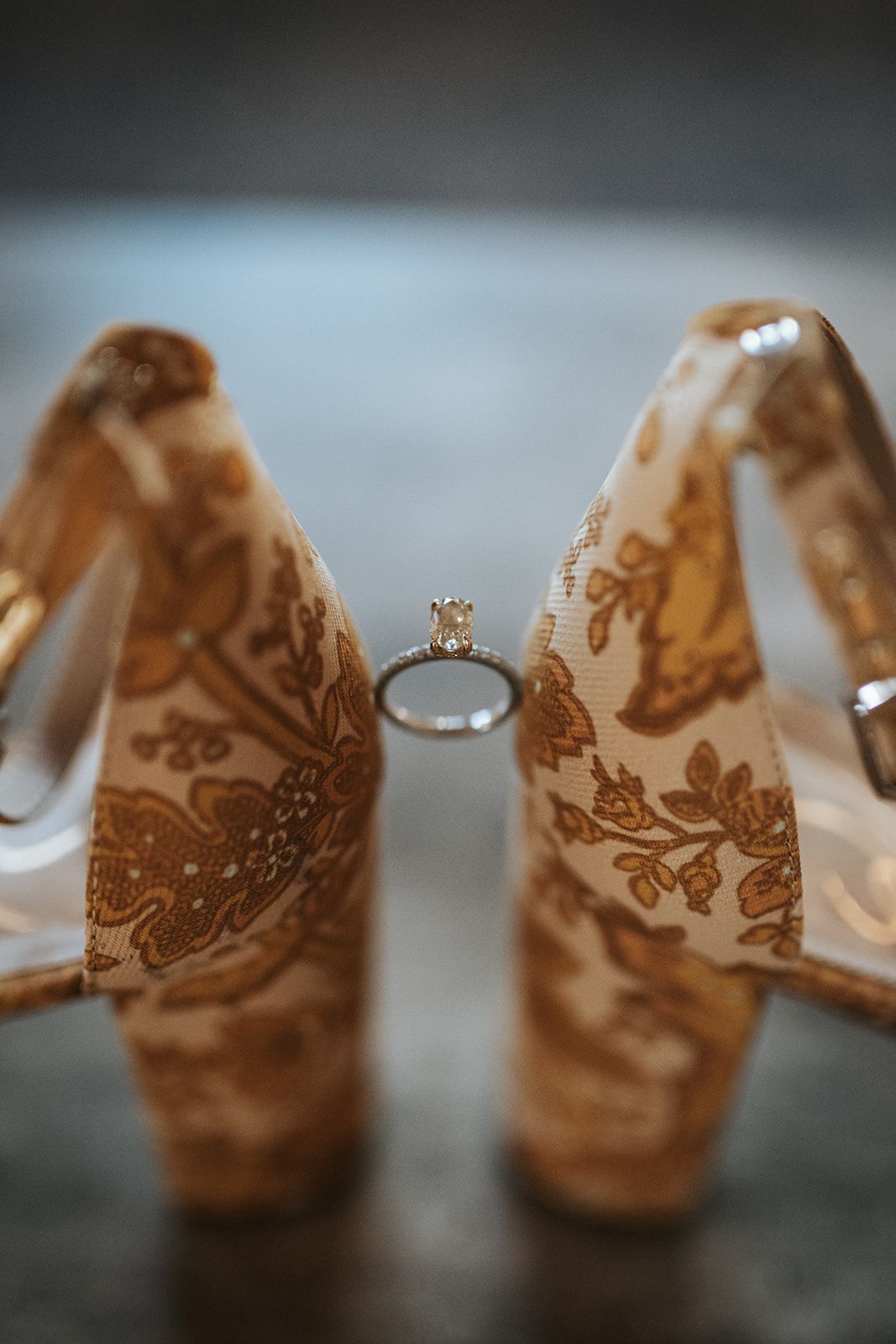 Gold lace high-heeled shoes framing a diamond ring on a dark surface