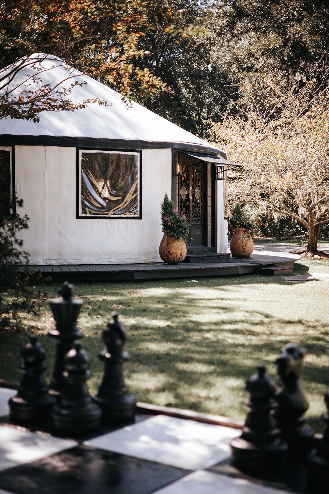White cottage with a thatched roof and potted plants beside a shaded lawn, with chess pieces in the foreground
