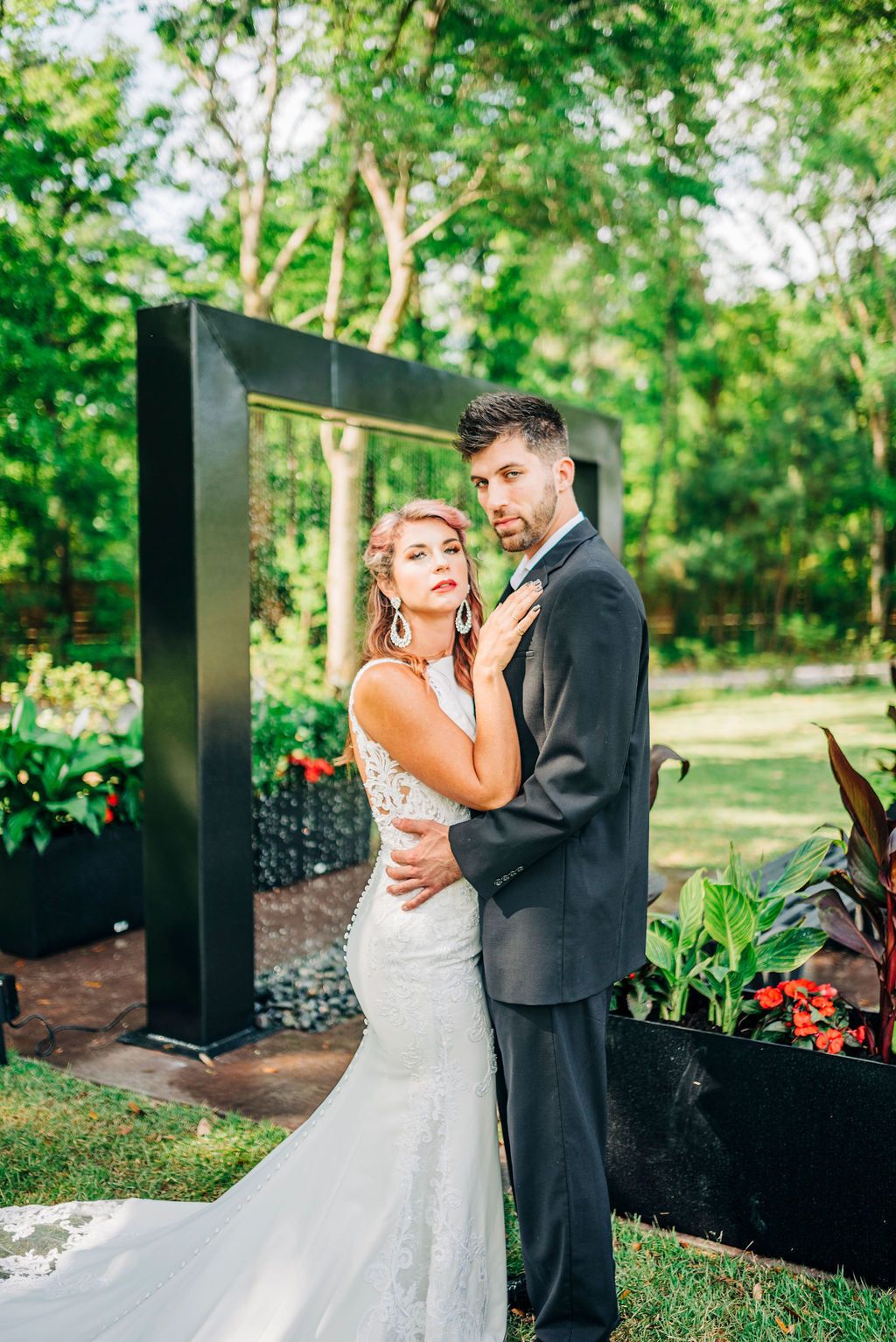 Bride and groom posing together outdoors near a black arch and flowers