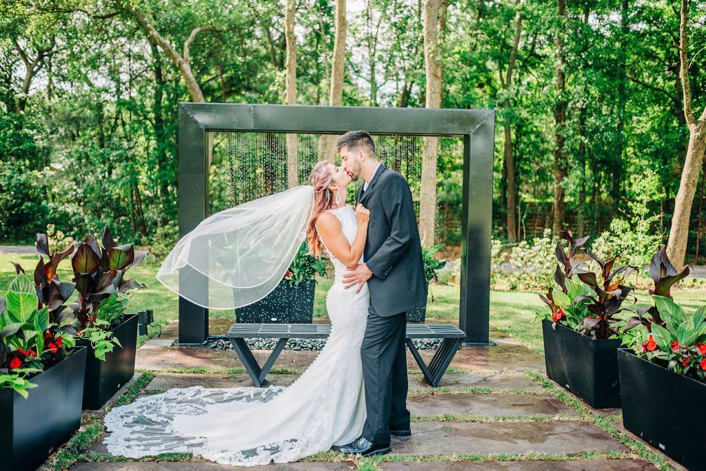 Bride and groom kissing under a floral arch in a lush garden ceremony