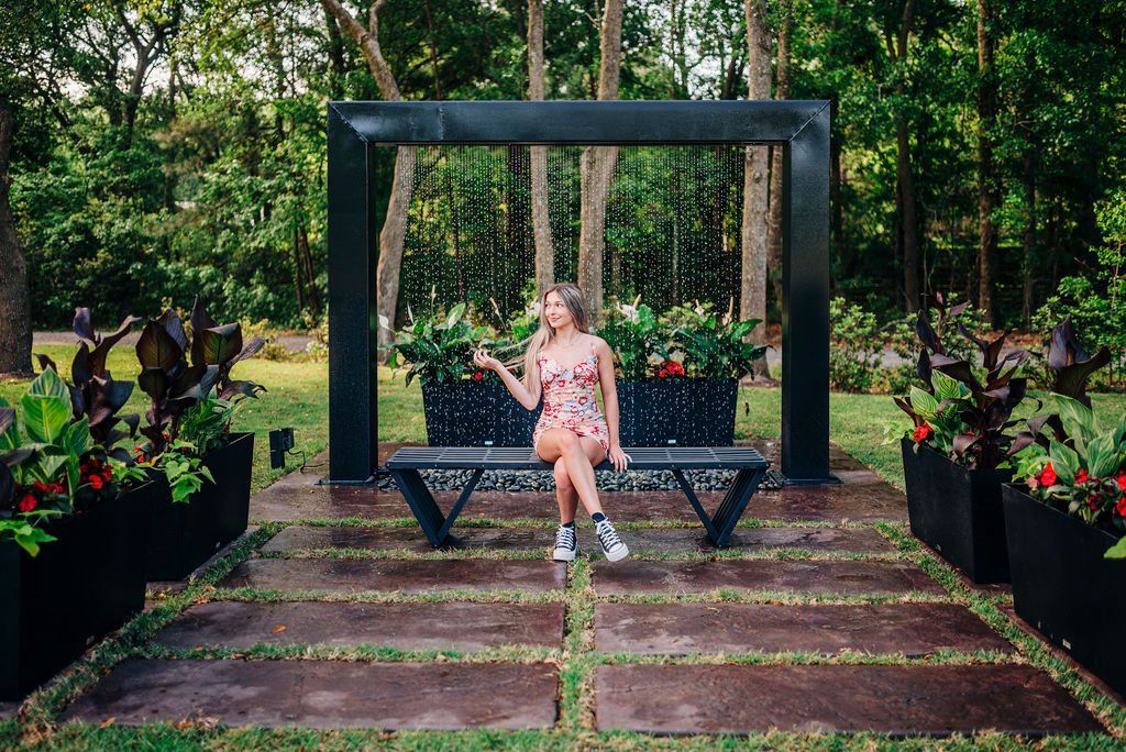 Woman in a pink dress sitting on a bench under a dark arch in a flower garden